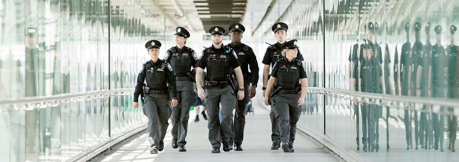 6 police officers of different backgrounds walk down a long glass hallway