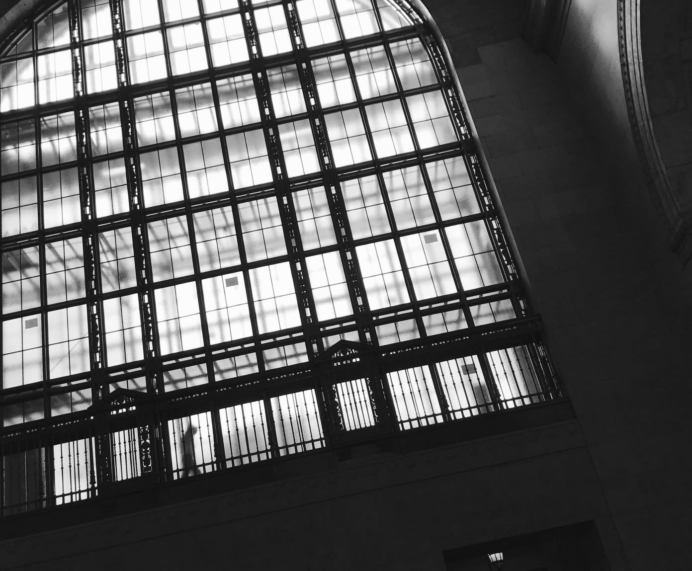 Looking up at high glass, a figure, behind it, is seen walking above Union Station. The glass is ...