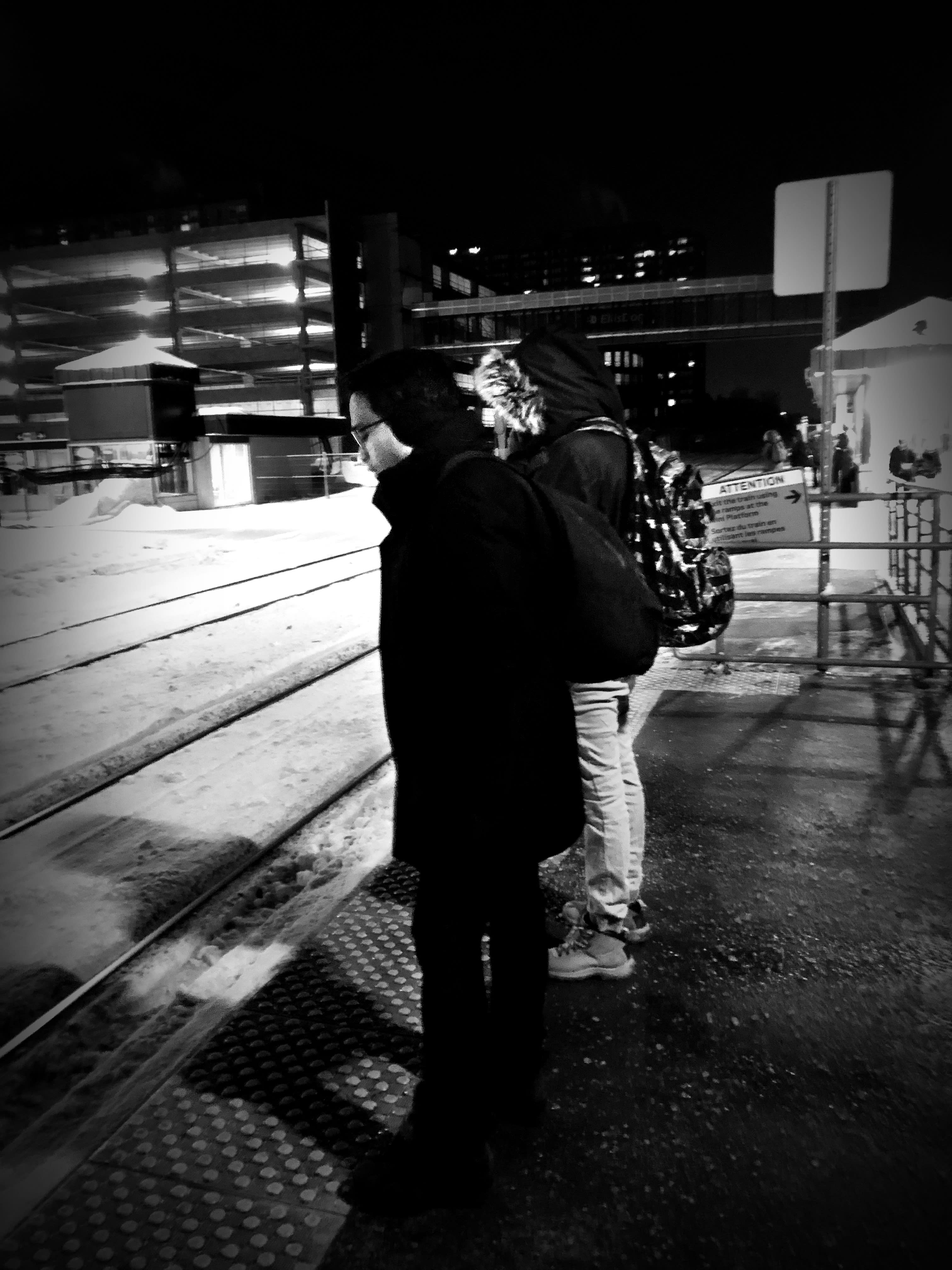 Two people stand in the cold while waiting for a train.