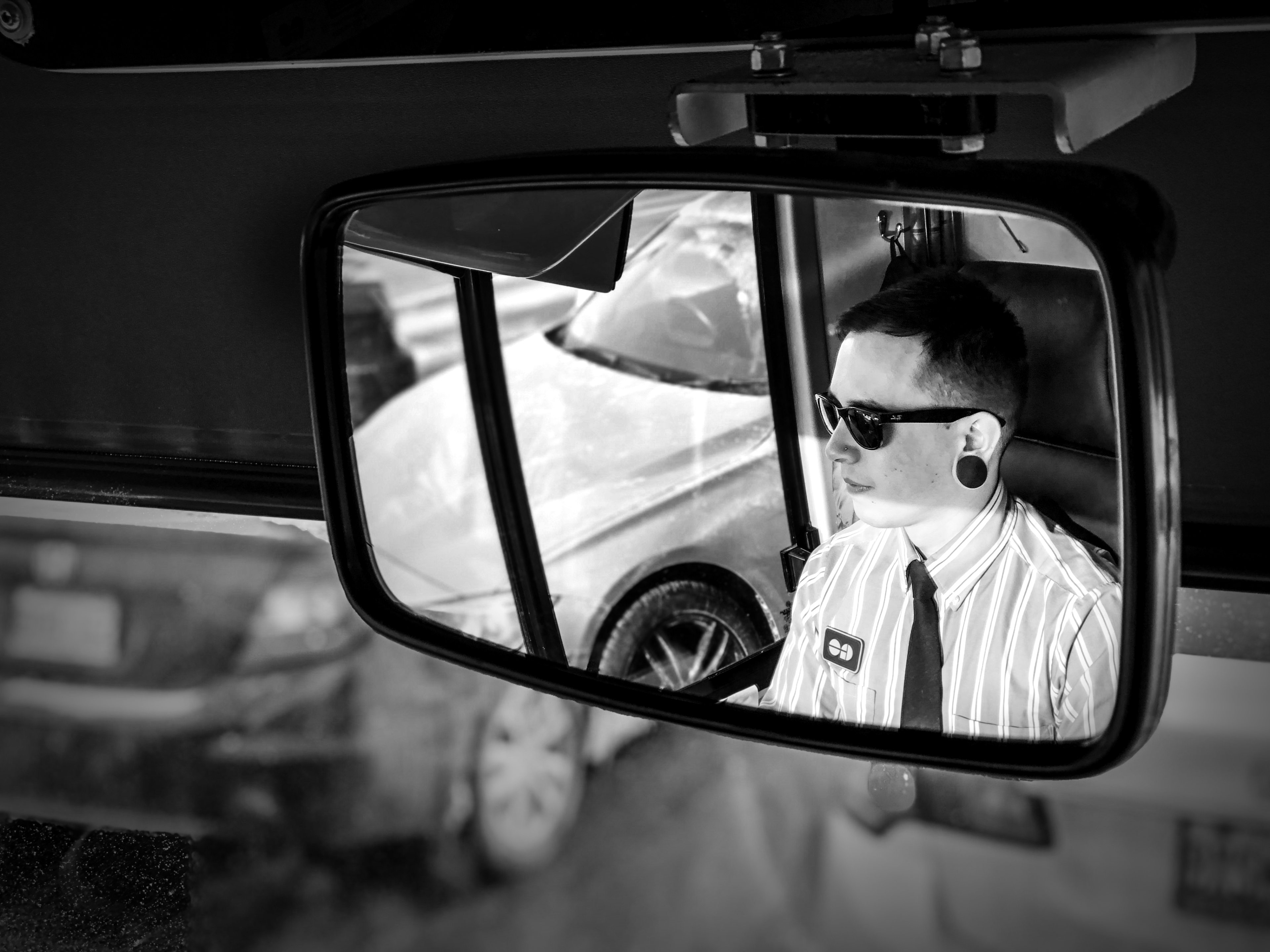 A bus driver is seen in a reflection of his mirror.