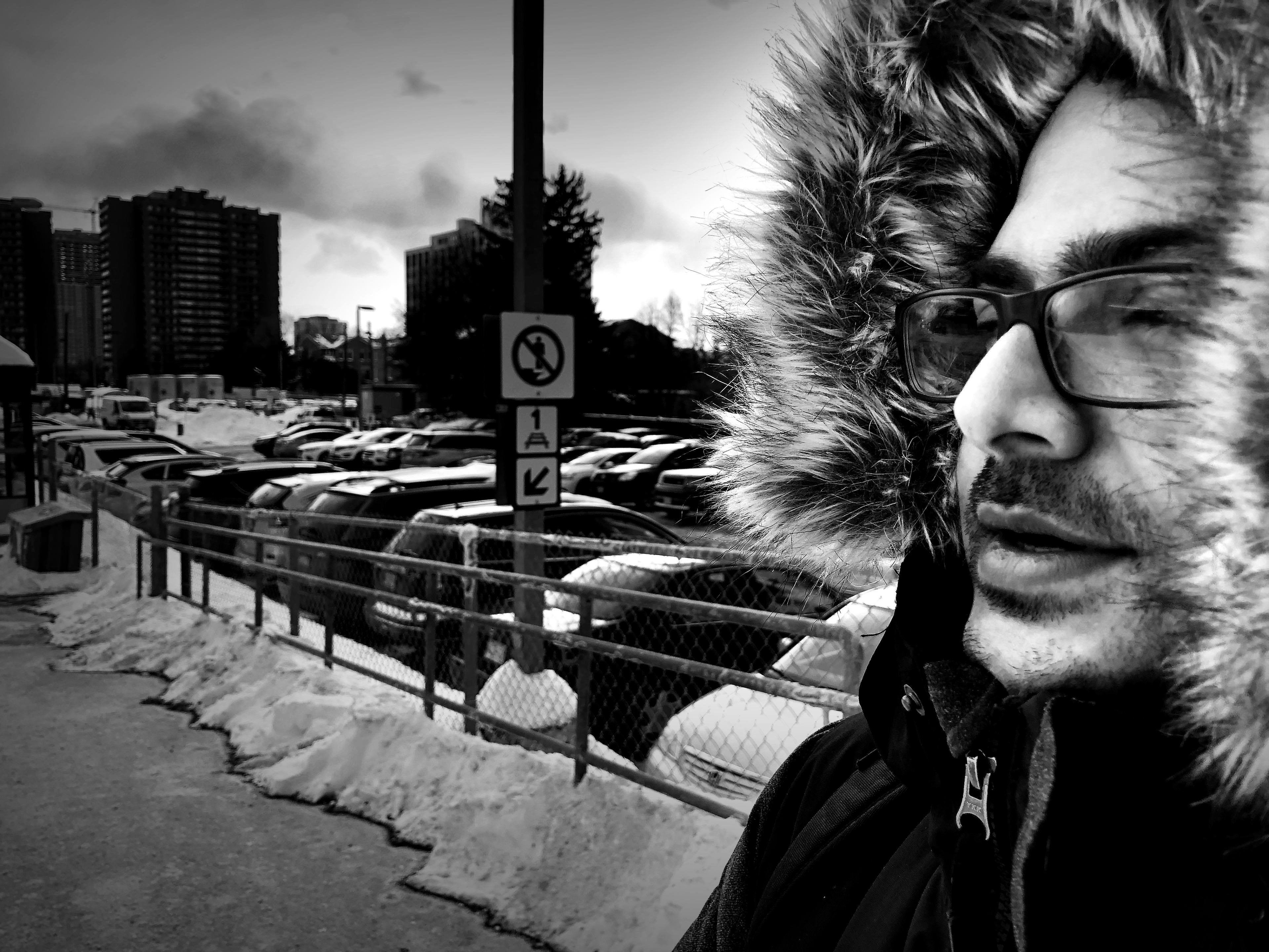 A man, bundled in a winter coat, breathes out into cold air as he waits for a GO Train.