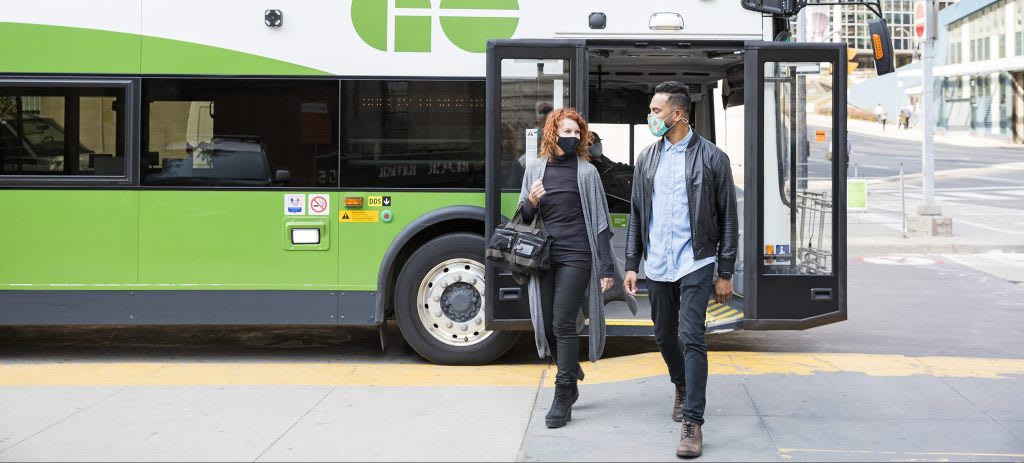 two people get off a GO bus with the yellow safety lines behind them.