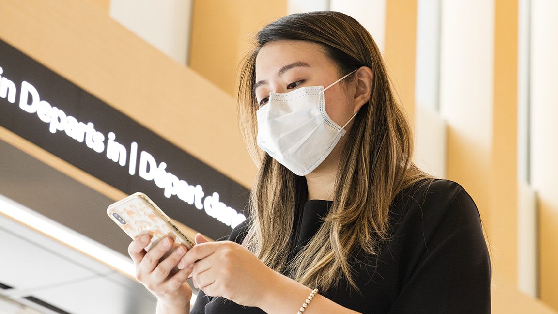 a young woman with a mask on looking at her phone