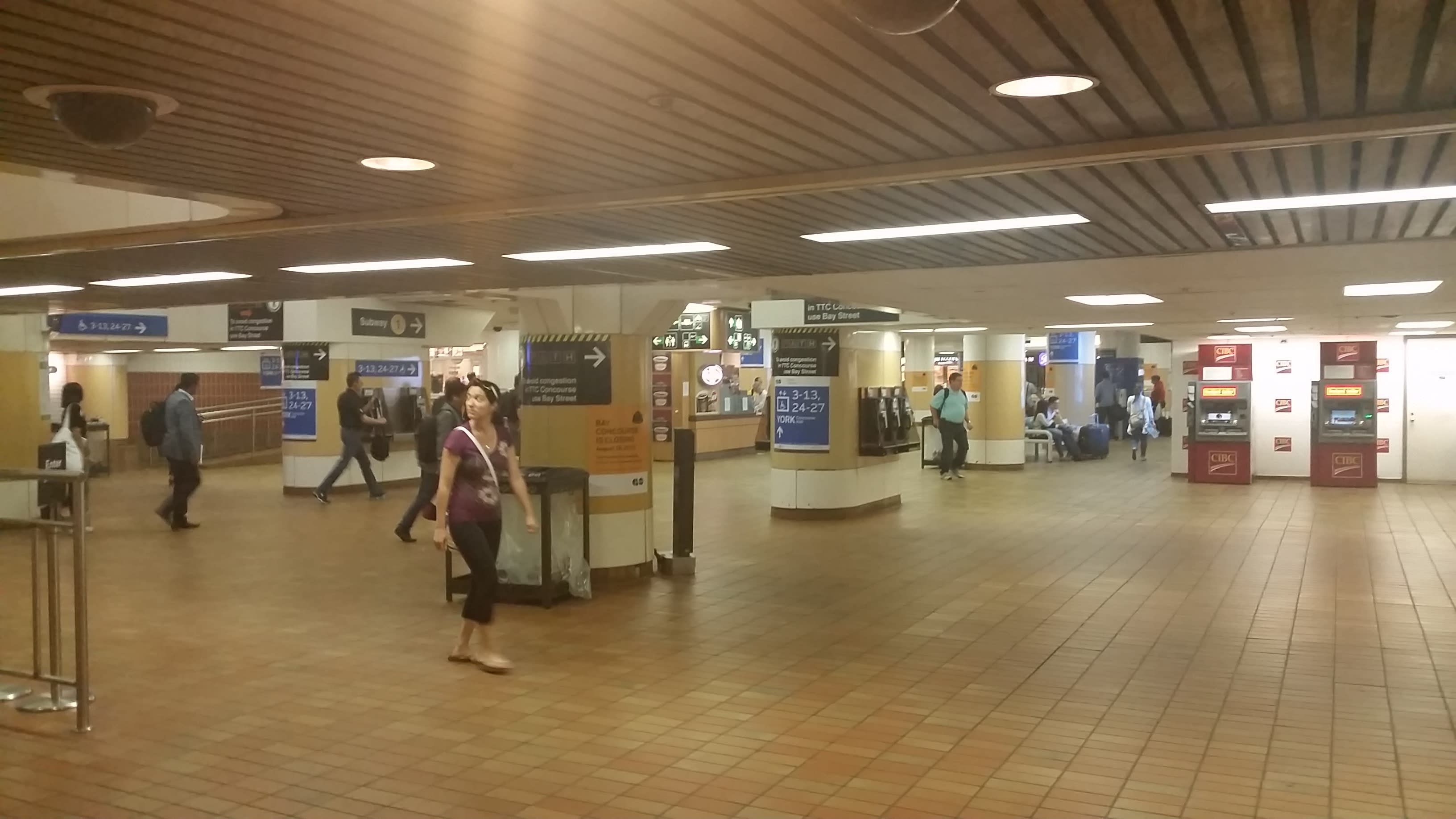 Customers walk through the halls of the old Bay Concourse. The ceiling is low and tile is brown.