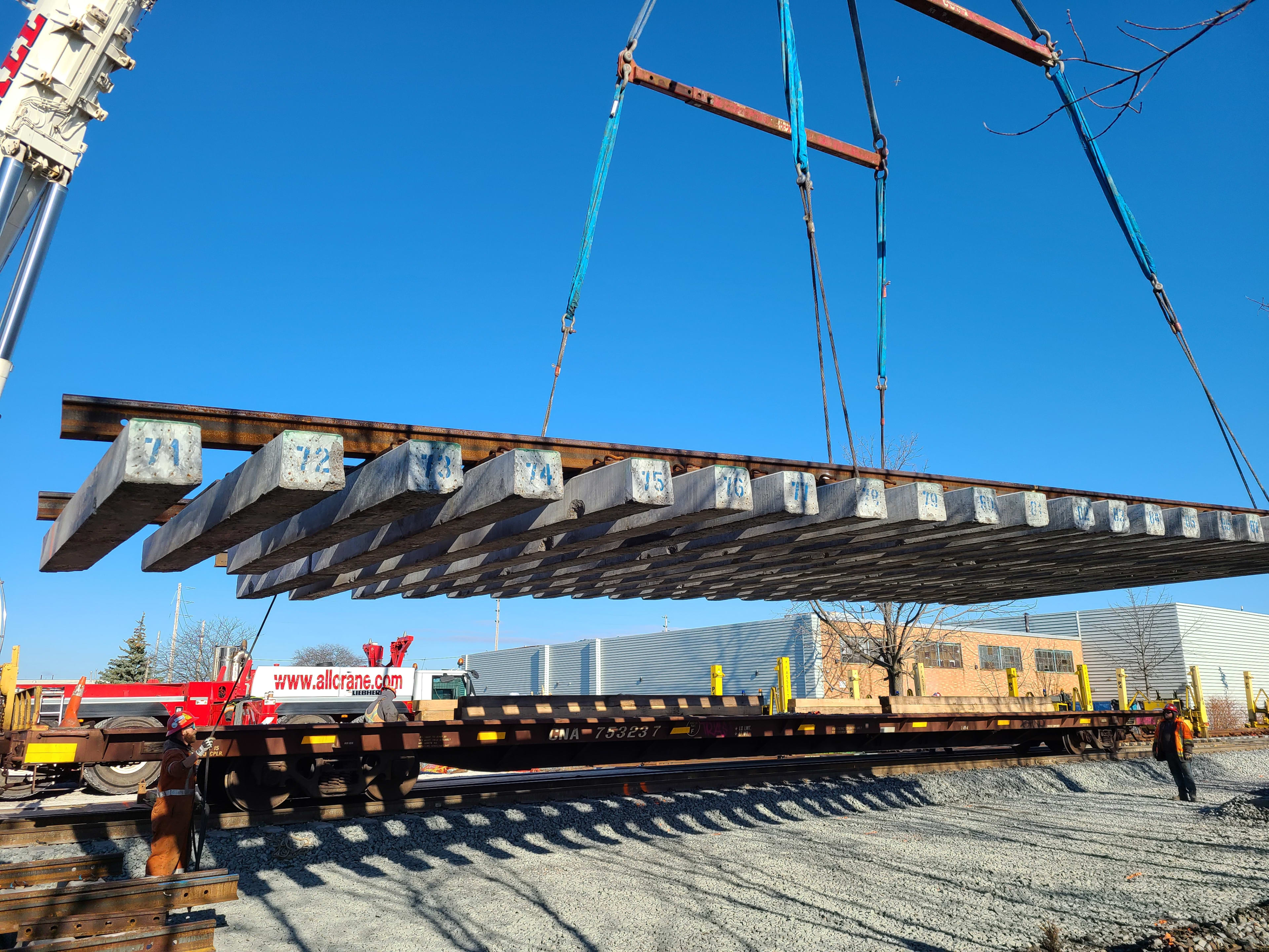 A large piece of track with concrete rail ties is lowered into place by a crane