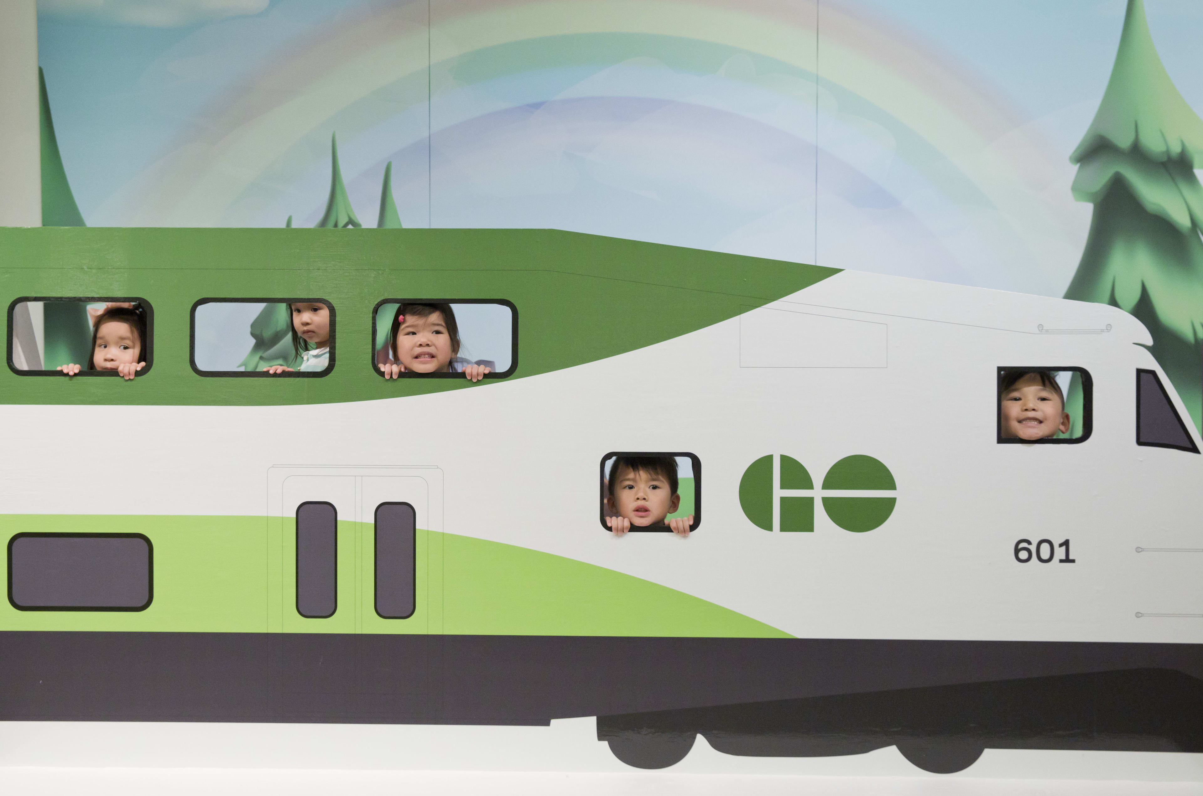 Children's faces are seen looking out of the windows of a small GO train display.