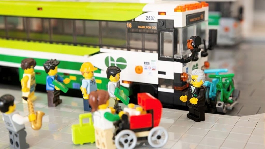 LEGO GO bus sit in model GO bus terminal with LEGO people waiting to board