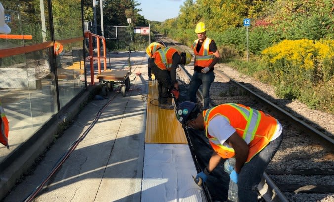 Construction crews installing yellow tactile strips on a GO station platform.