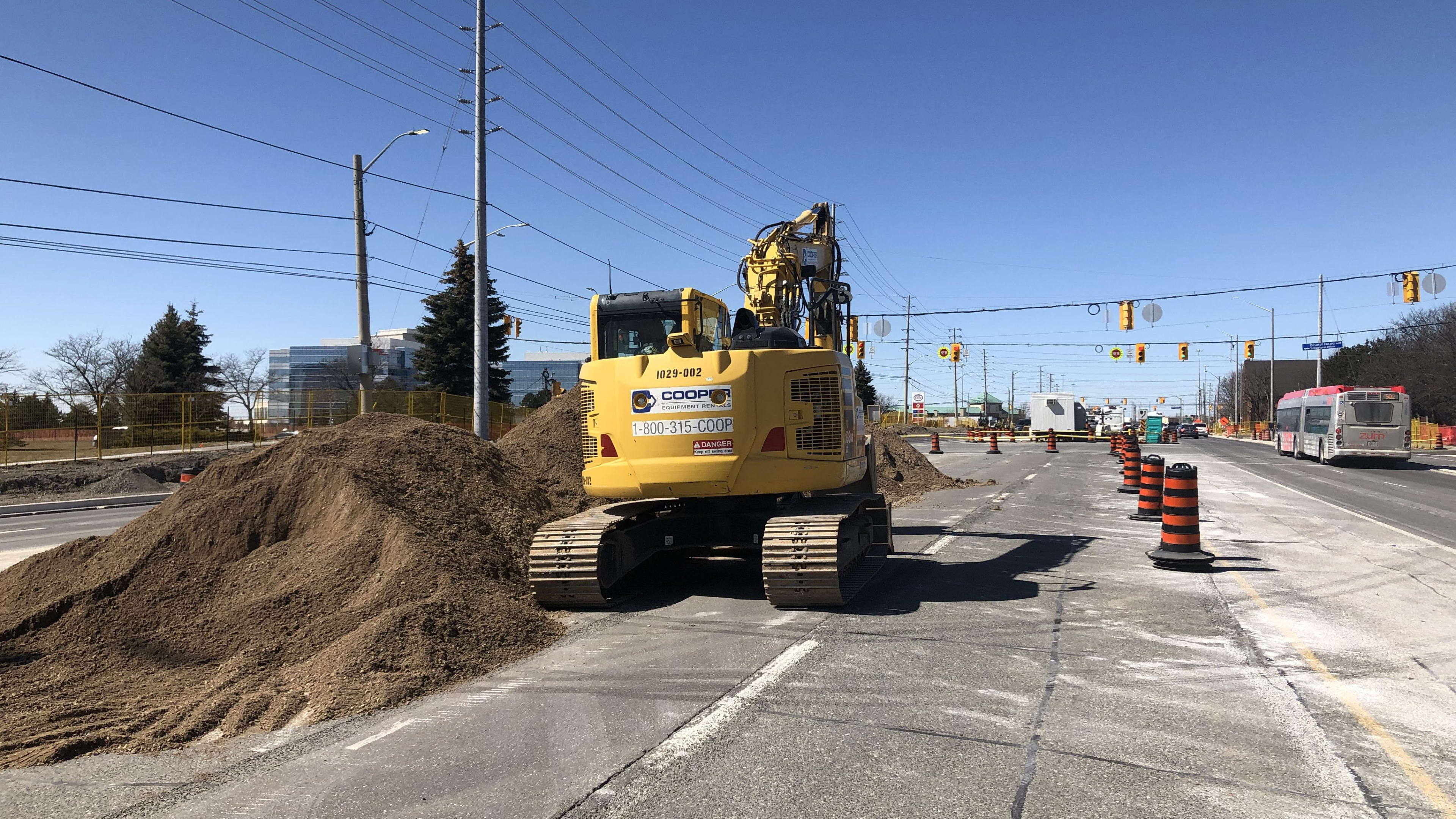 An excavator in the middle of the road working with a pile of dirt