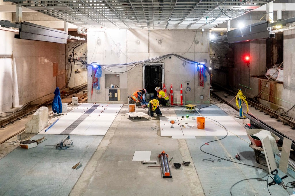 crews hard at work installing the white tiles at Leaside Station that will cover the floor at pla...