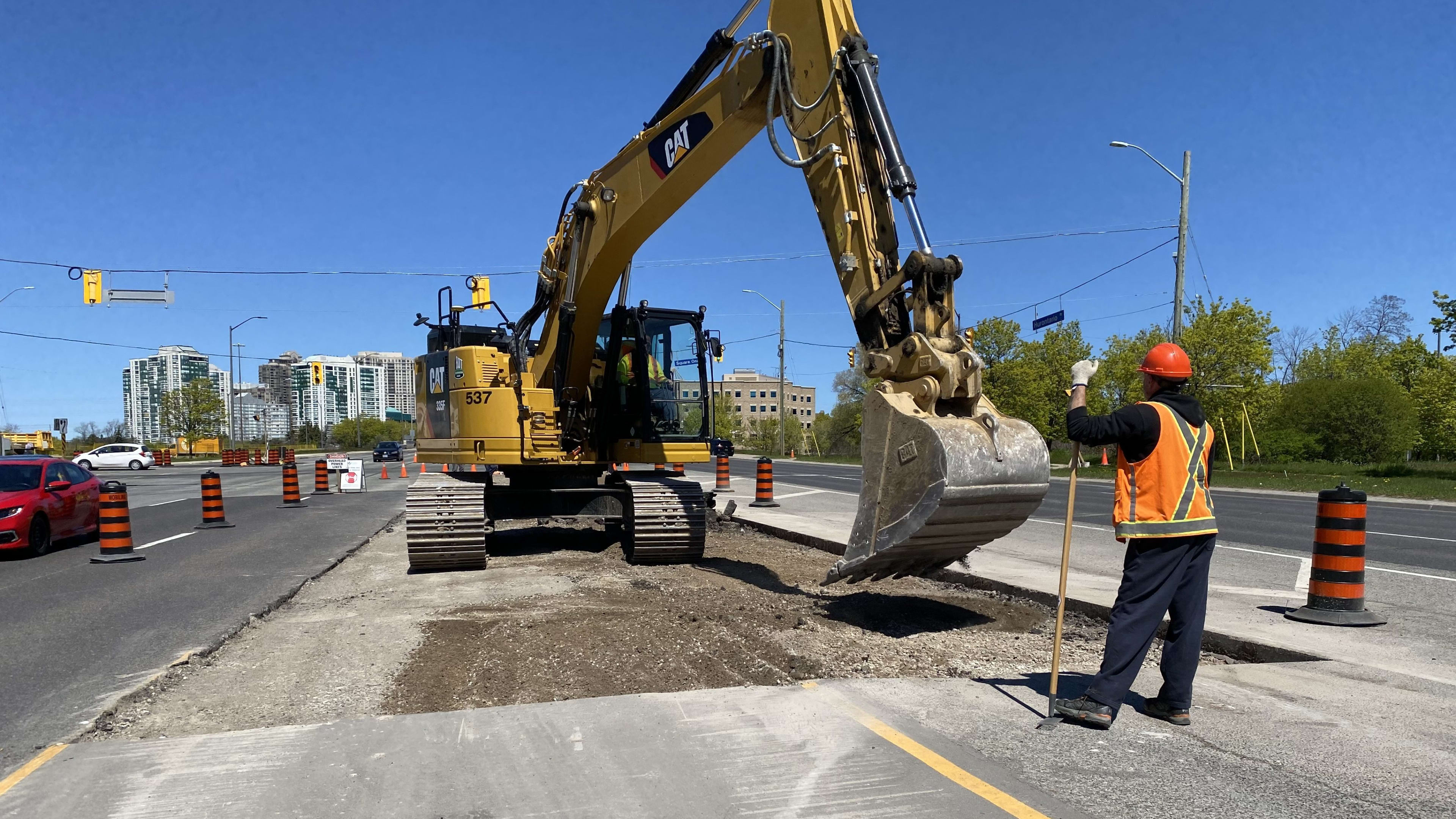 An excavator works along Hurontario while a construction worker looks on