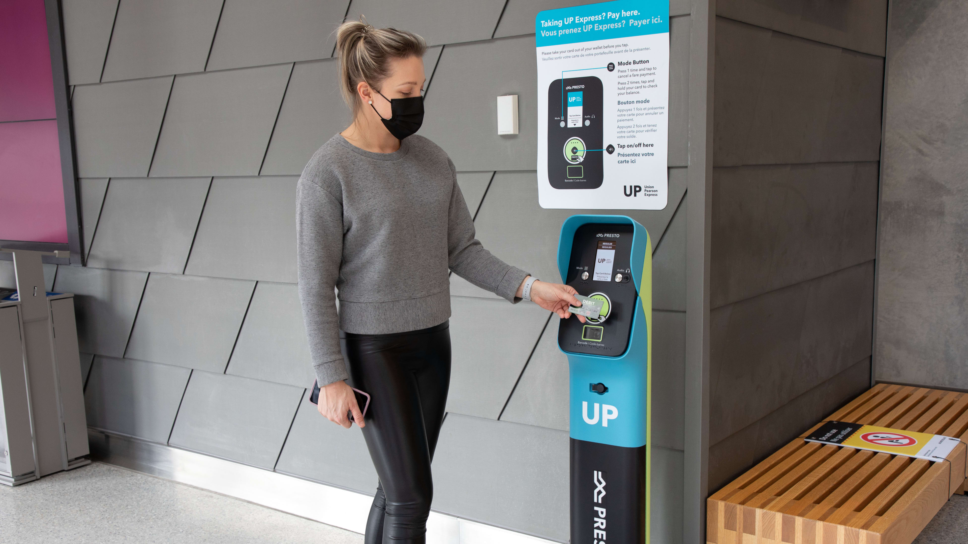 A woman in a mask taps a presto card on a UP Express machine