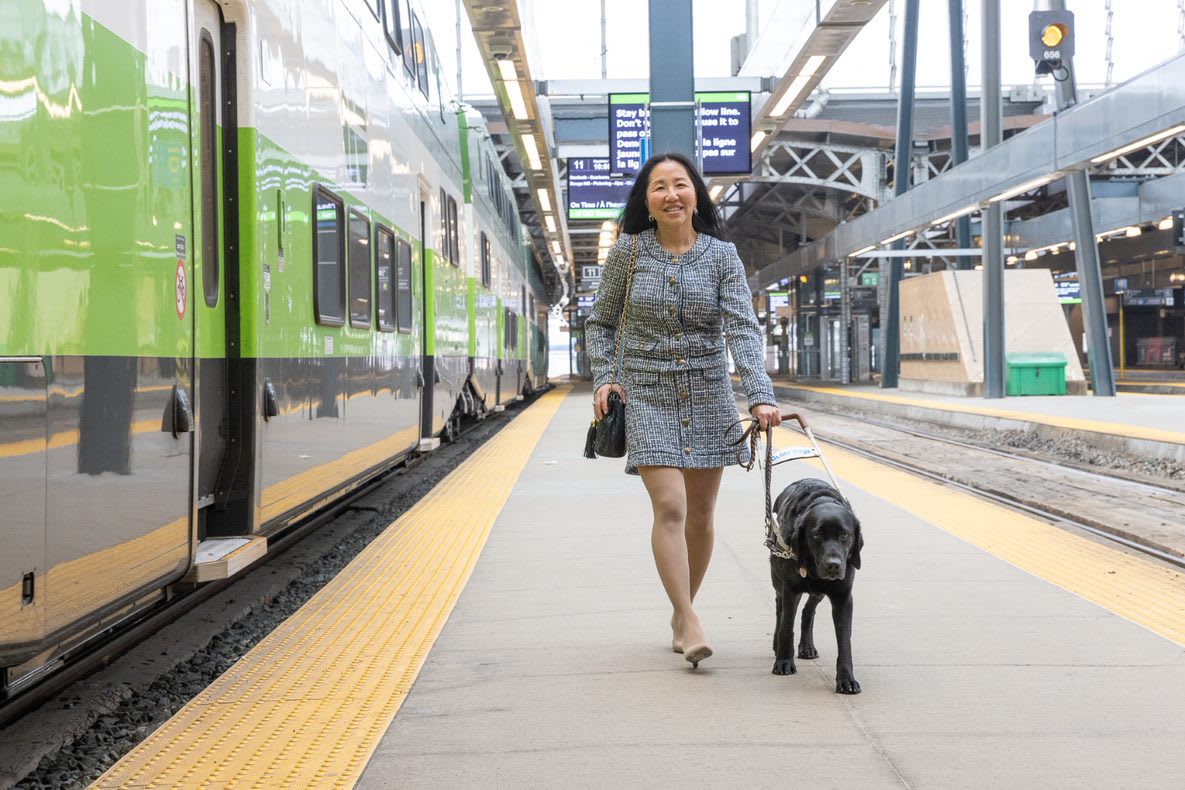 A woman walks with a service dog on a train platform