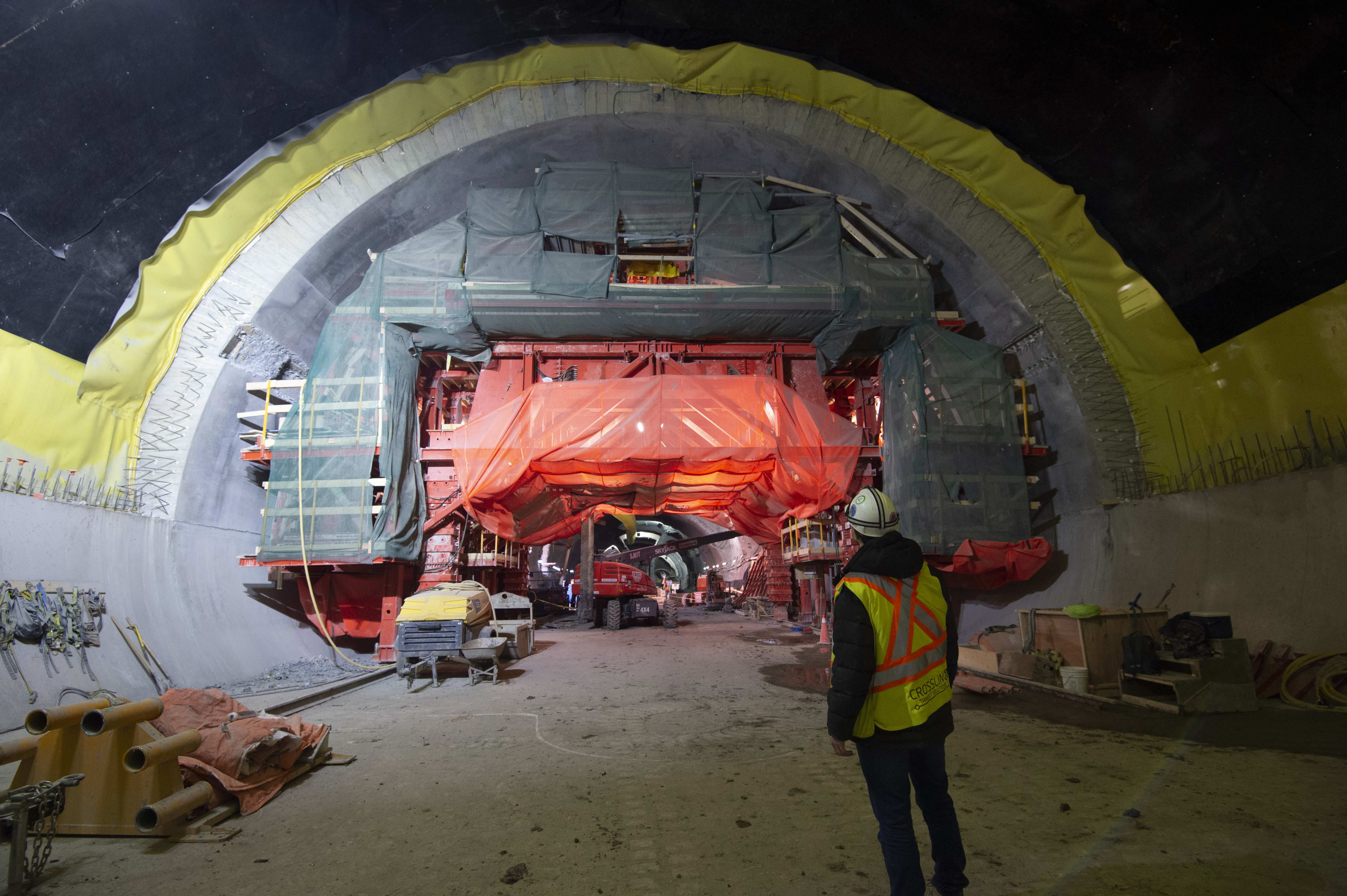 A workman looks at a large concrete tunnel, with equipment working inside.