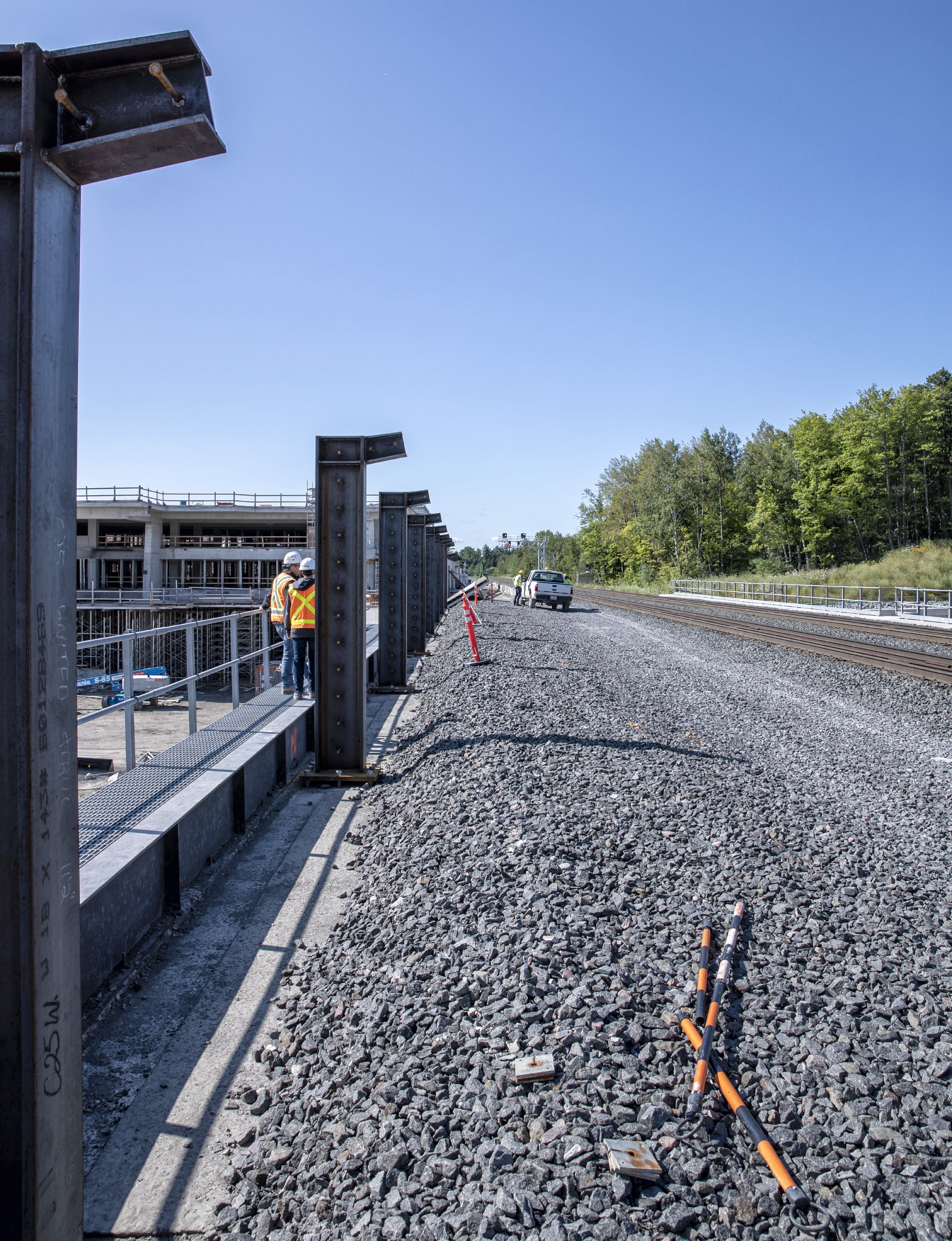 A gravel bed supports rails, as workmen toil nearby.