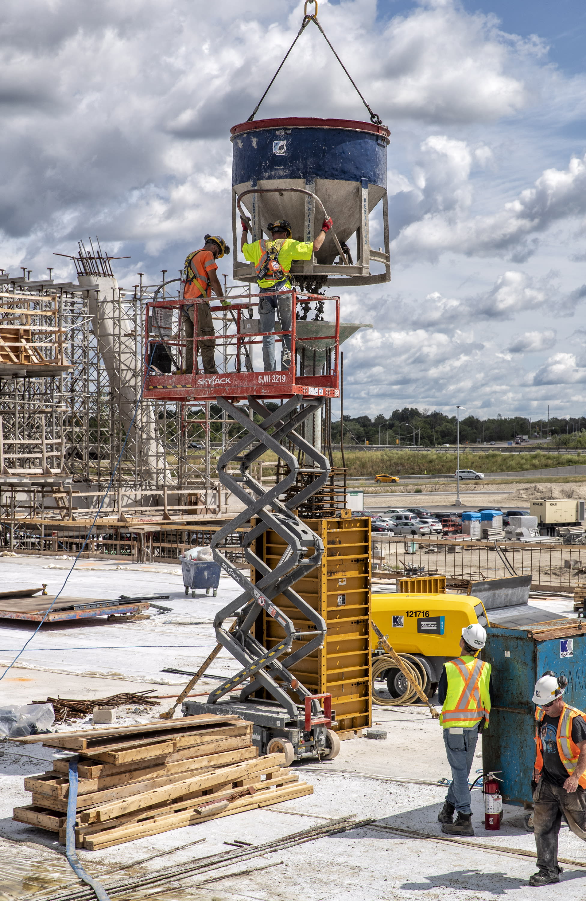 Construction workers lower a concrete bucket into place with use of a sky jack.