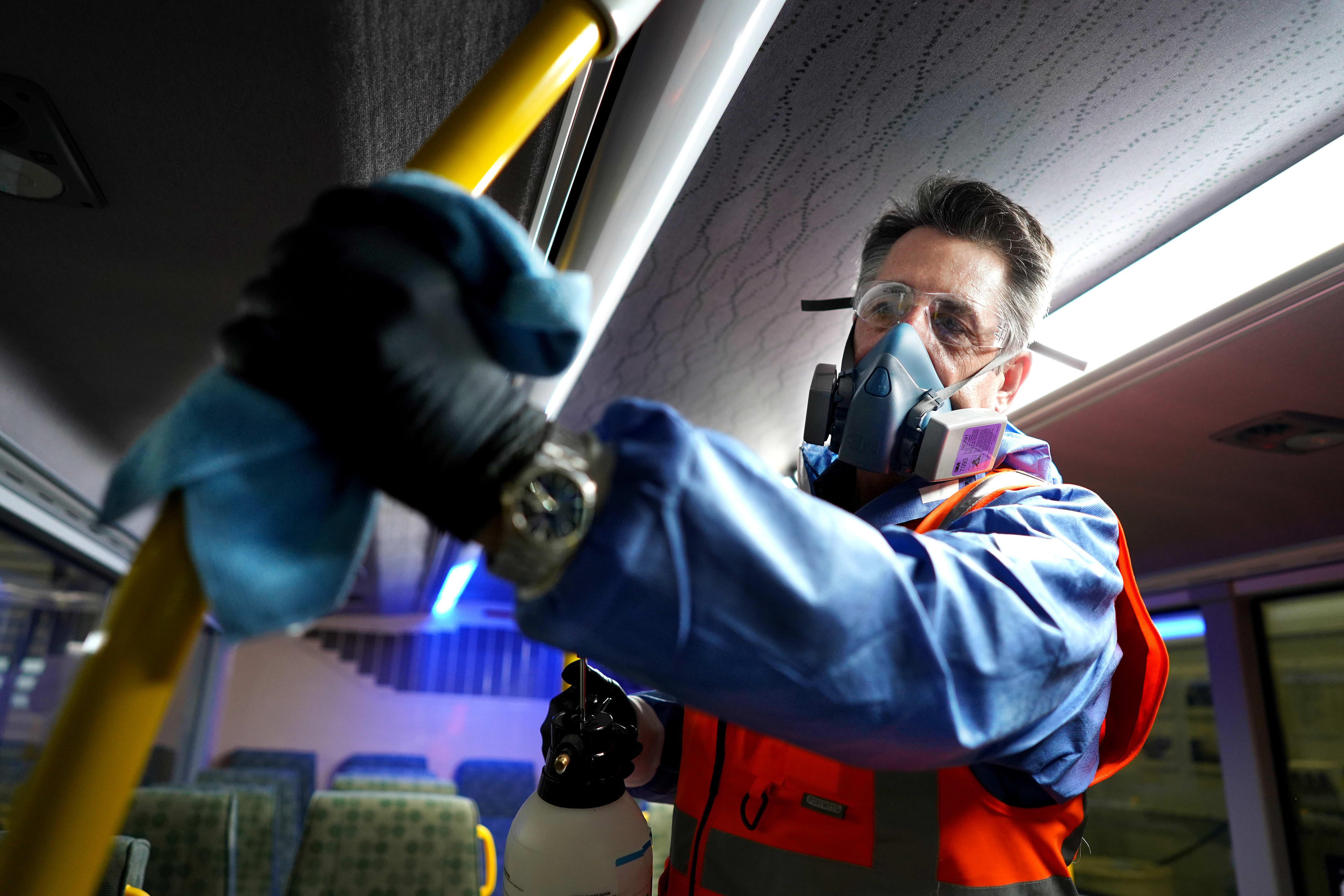 A cleaner used a rag to wipe down a handle bar. He's wearing a mask and gloves.