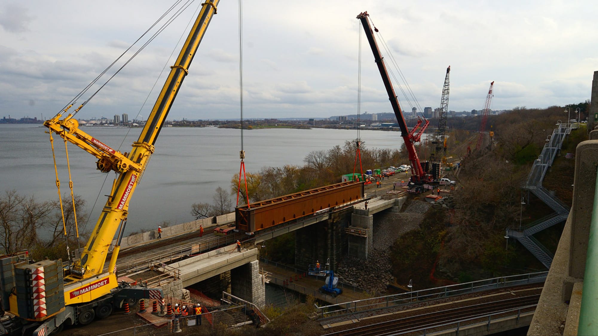 Cranes lift a large piece of steel into place during construction on a rail bridge at the Desjard...