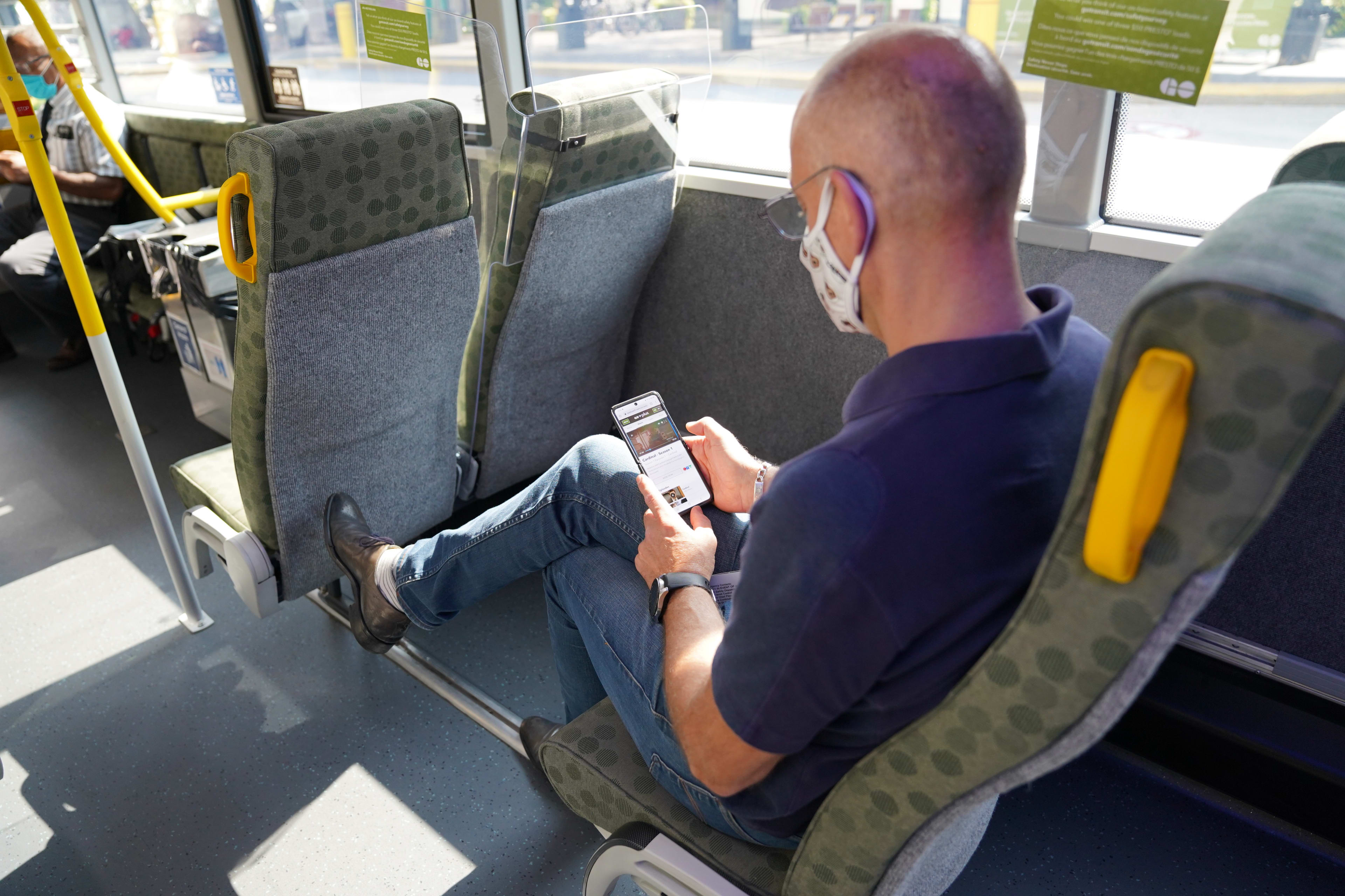 A man sits on a GO bus and looks at his phone.