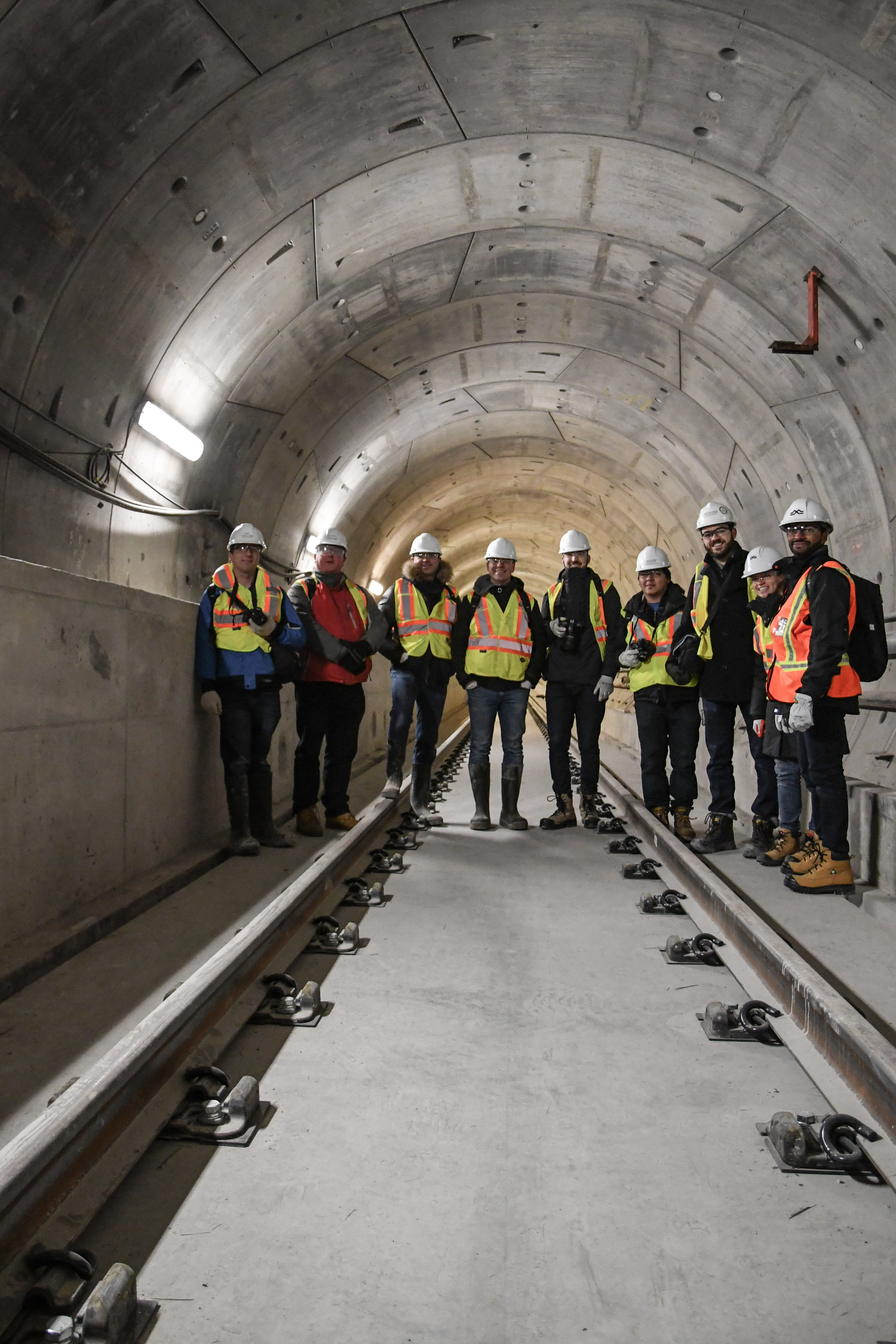 Nine people pose and look at the camera while standing on track and in a large concrete tunnel.