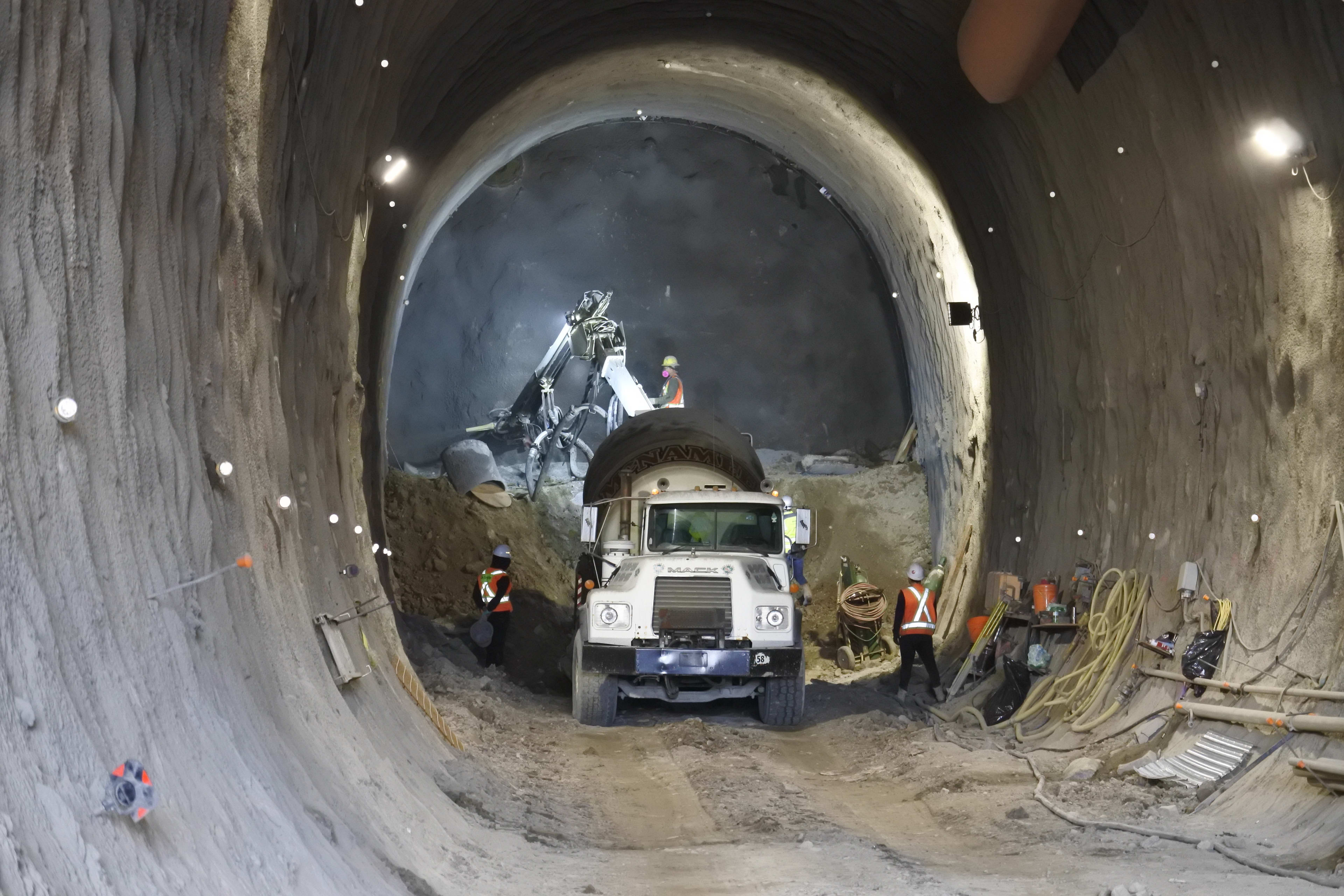 a tunnel, with crews working by worklights inside.