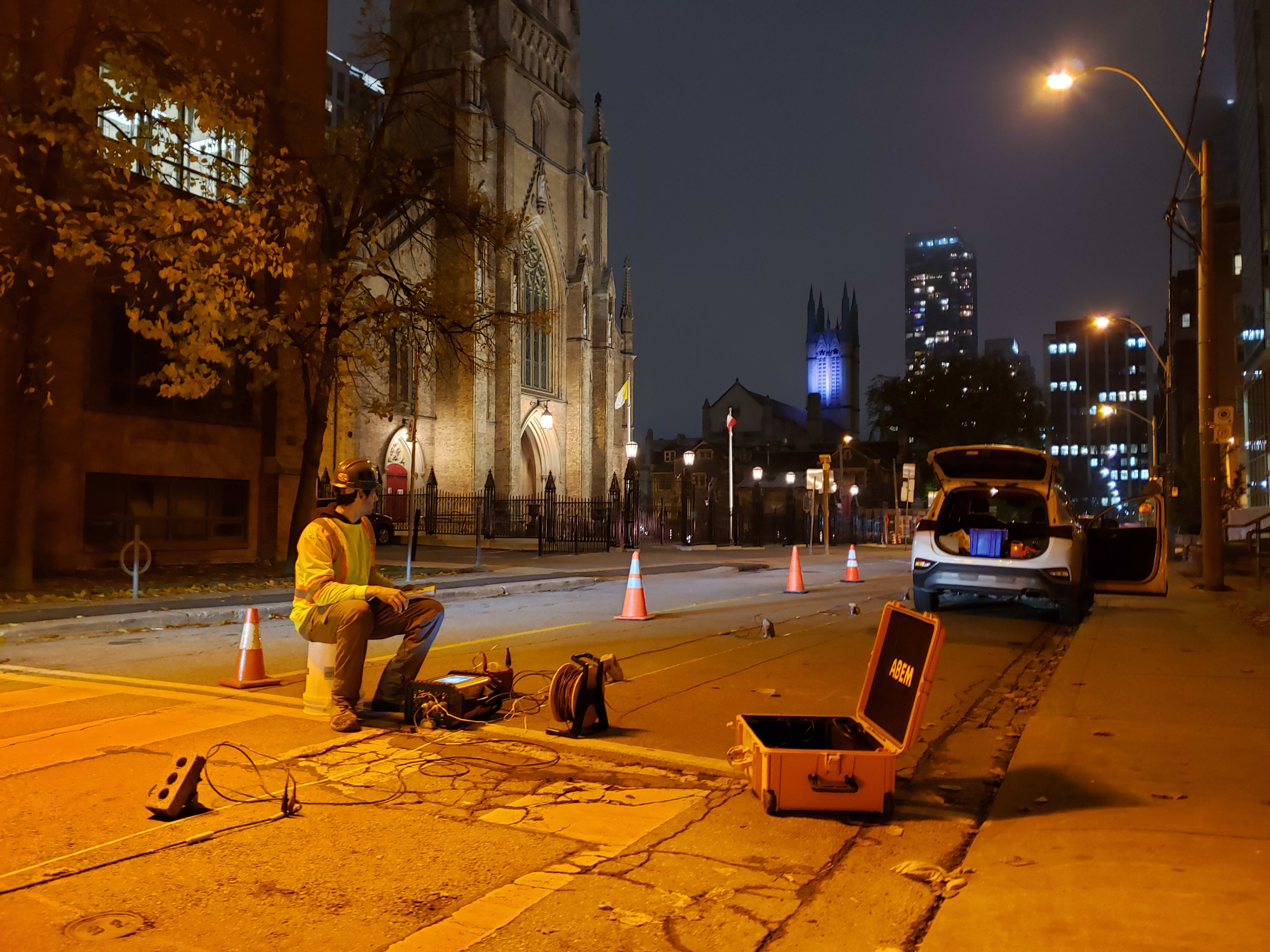 A person sits on a stool and looks at a monitor while in the middle of a street.