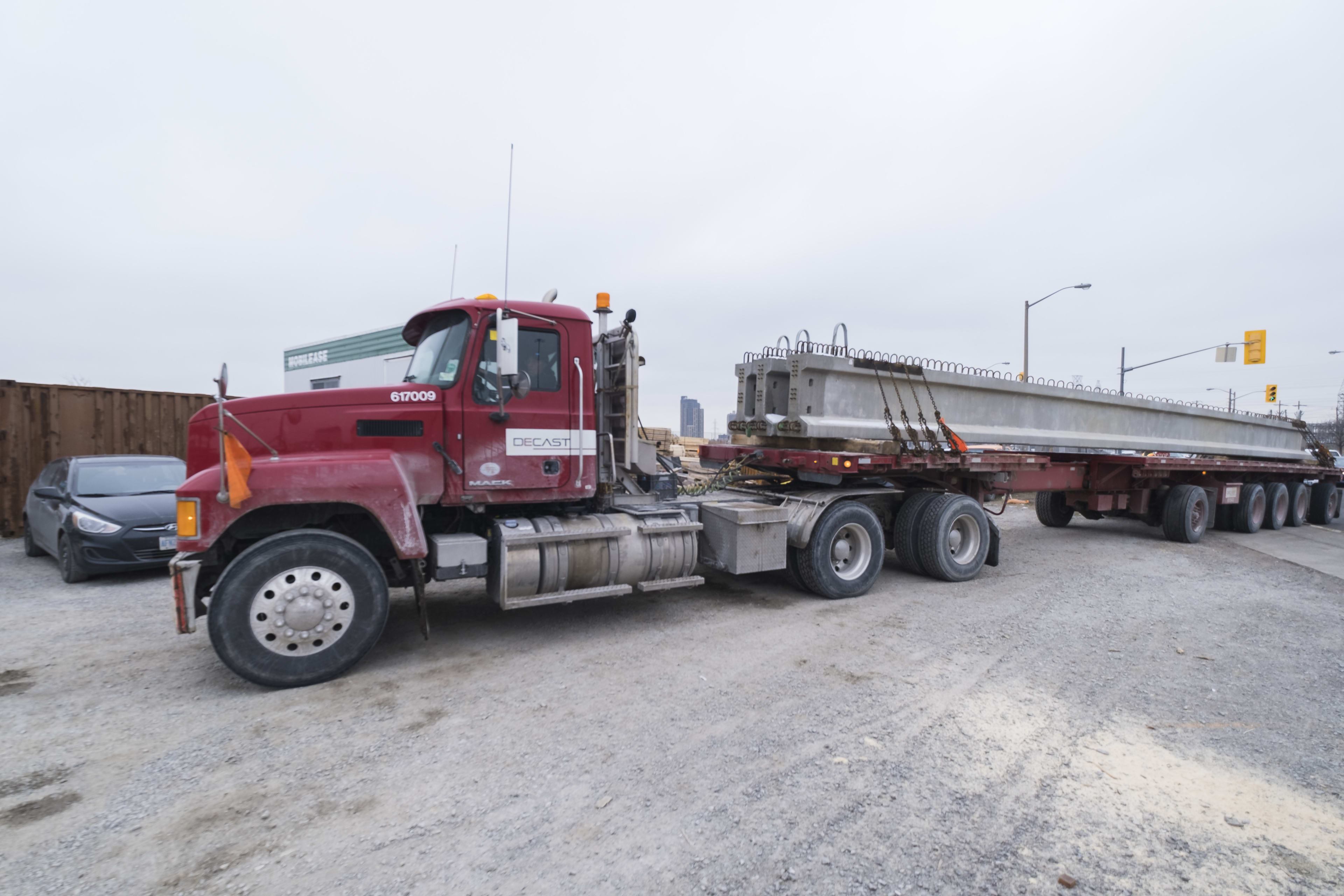 A truck hauls in large concrete girders.