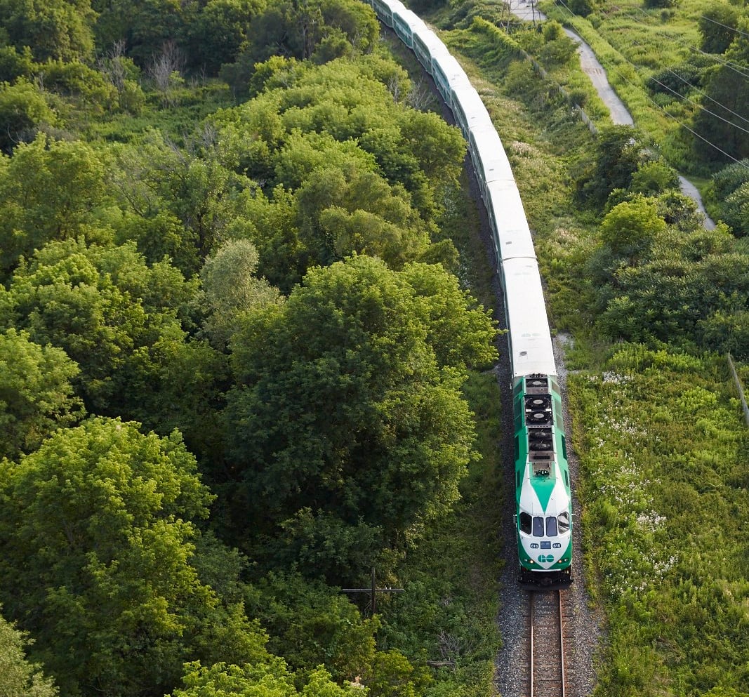 A GO train moves through a wooded area, aerial view