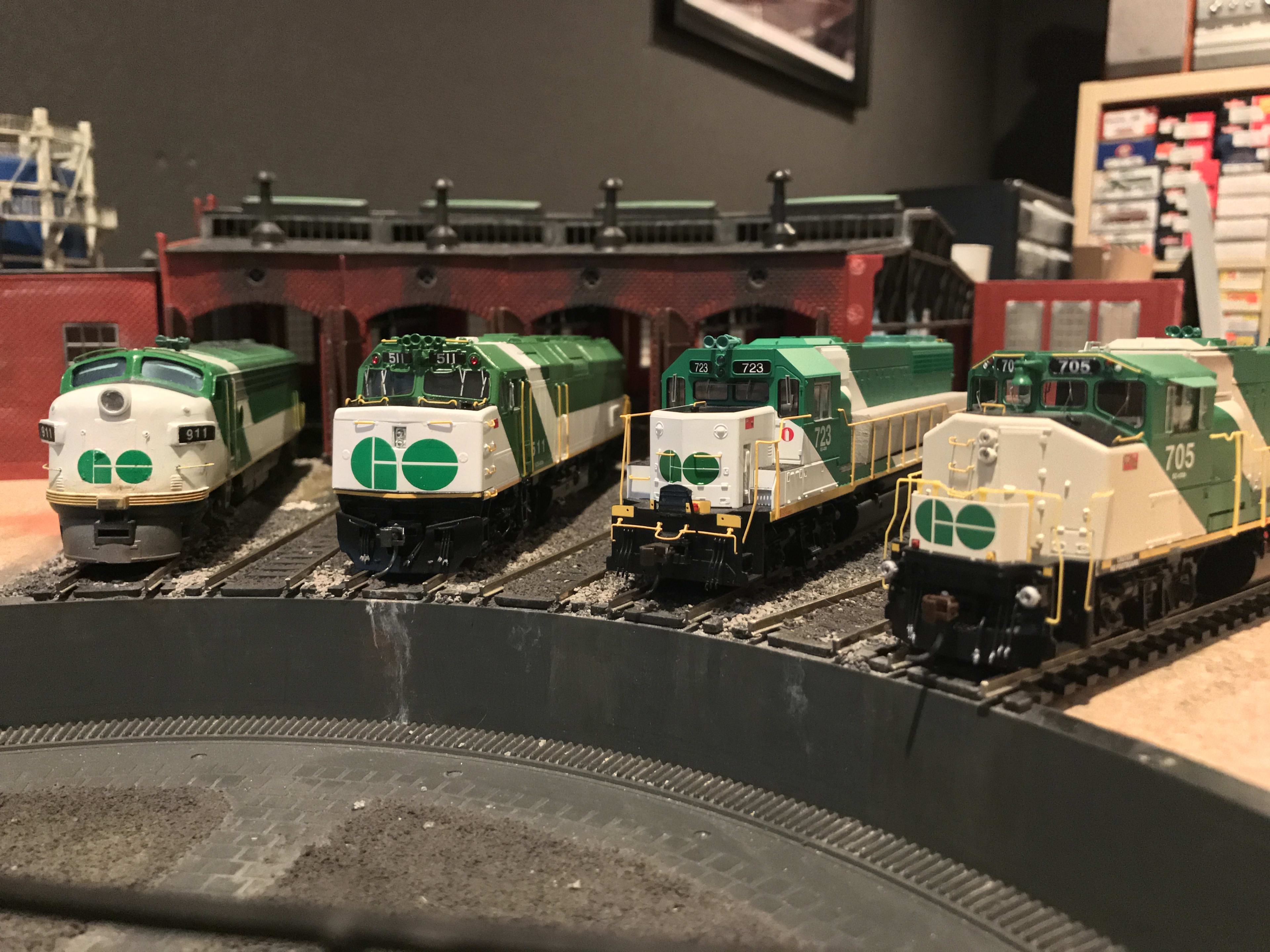 four model GO trains sit idle in the miniature rail yard.