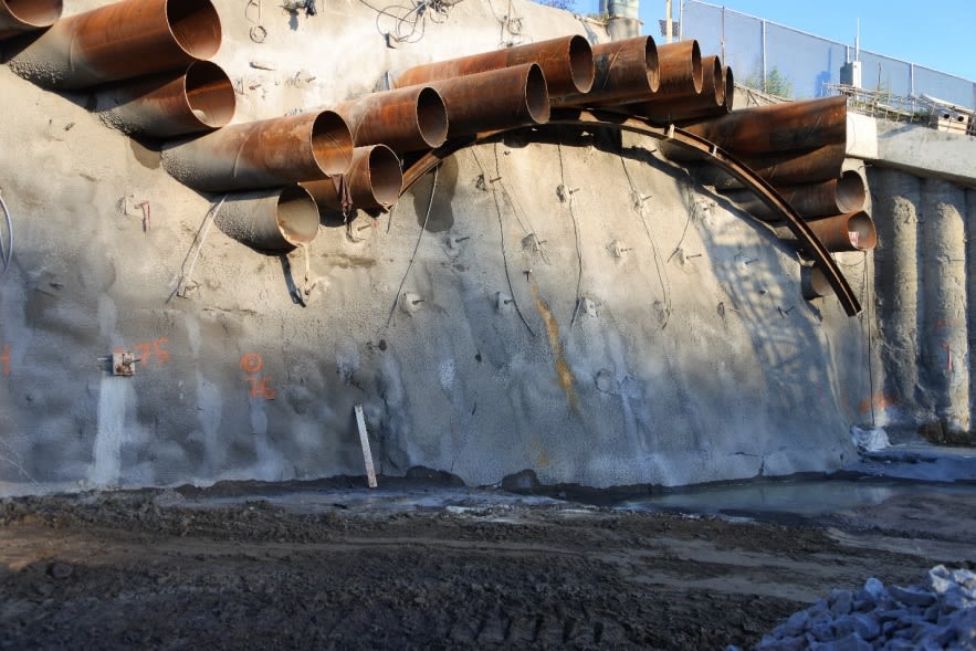 Large pipes extend out from concrete at the side of the tunnel.