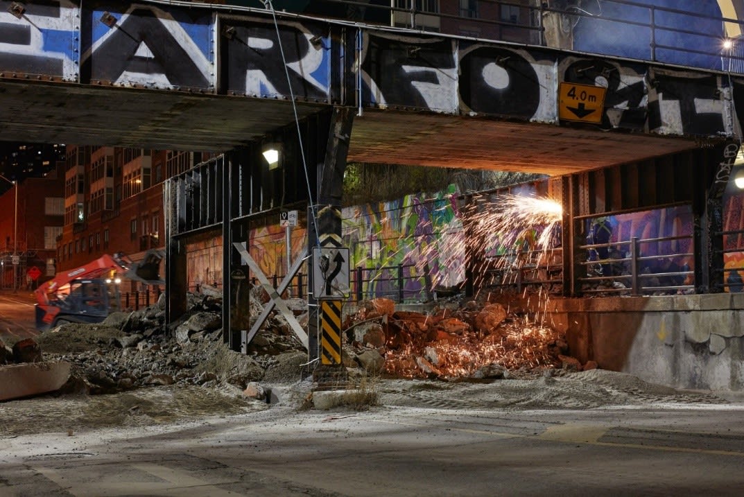 Workers cut metal with a torch under the bridge.