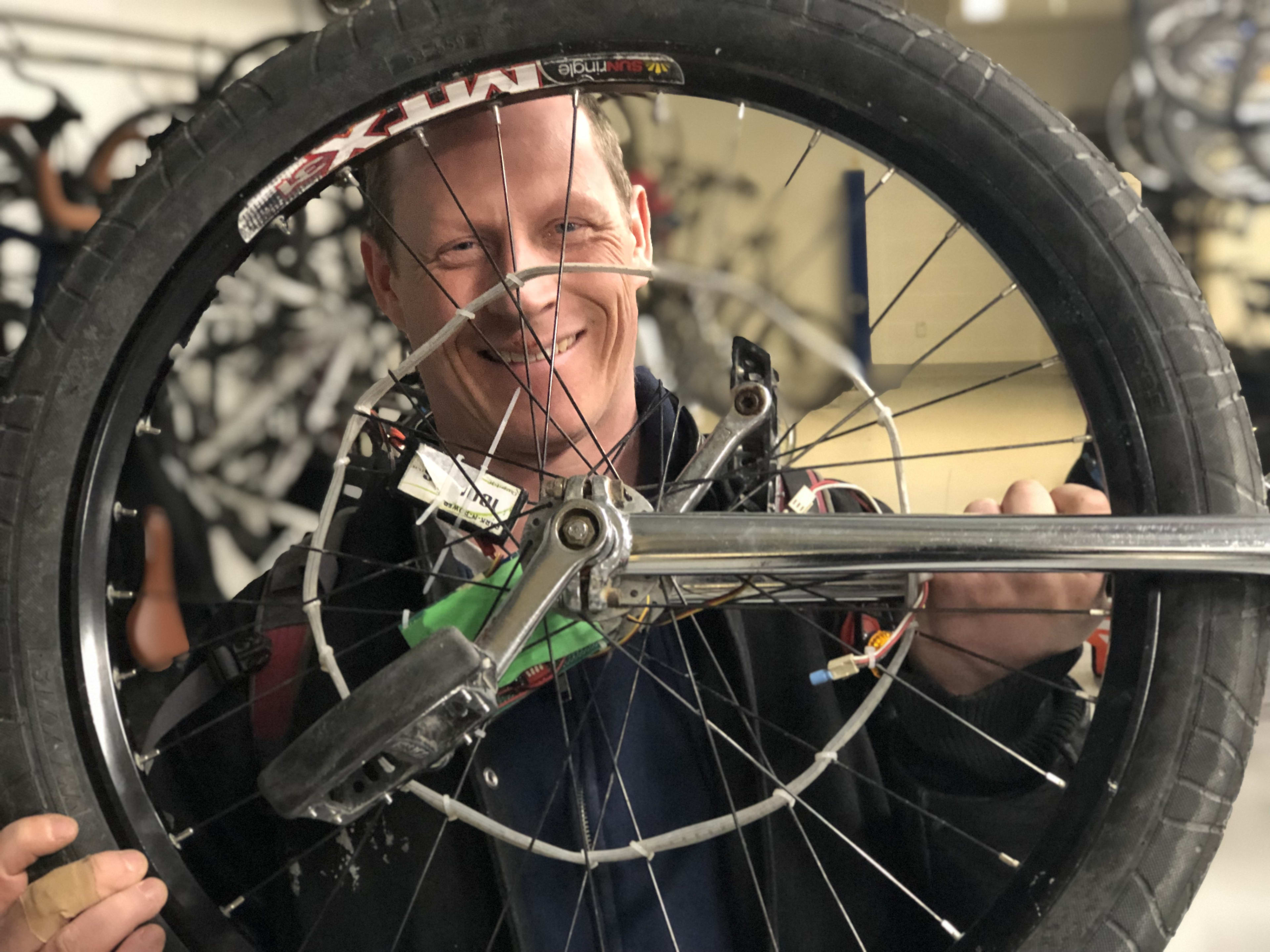 Ryan McArthur is shown looking through the spokes of his unicycle, as he stands inside the bike l...