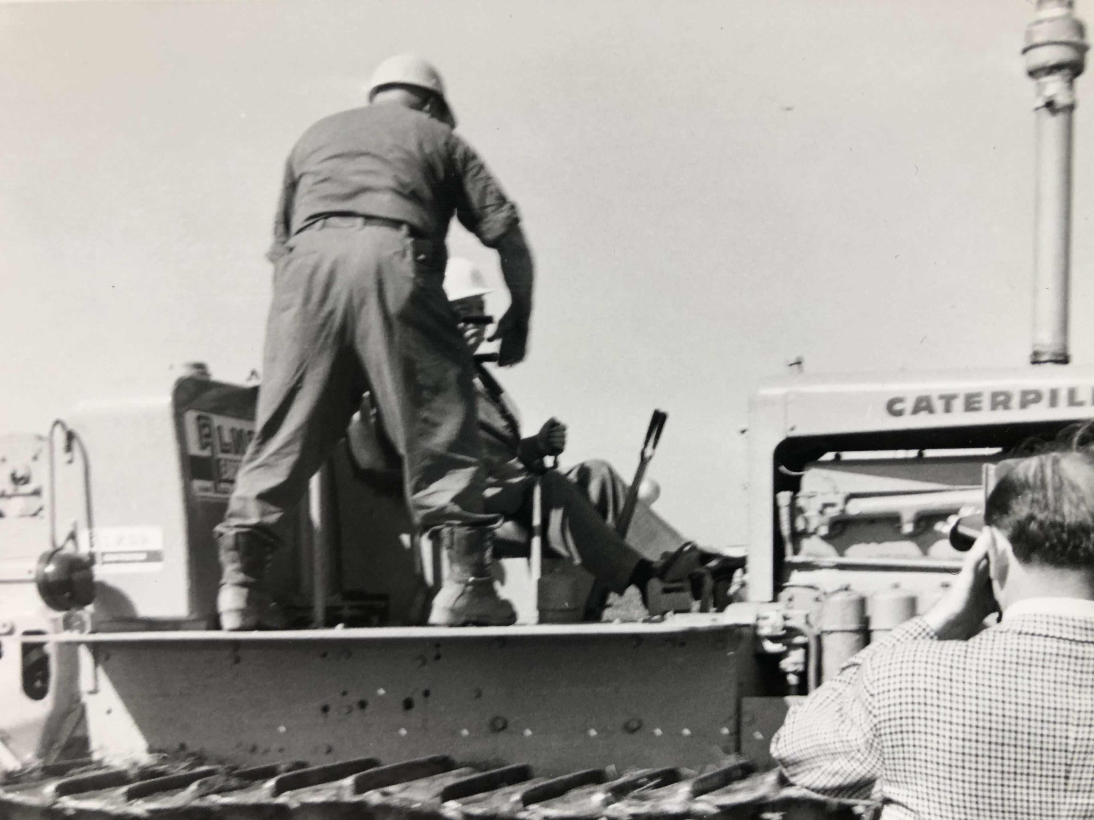 Two men sit on a tractor as one prepares to move it forward.