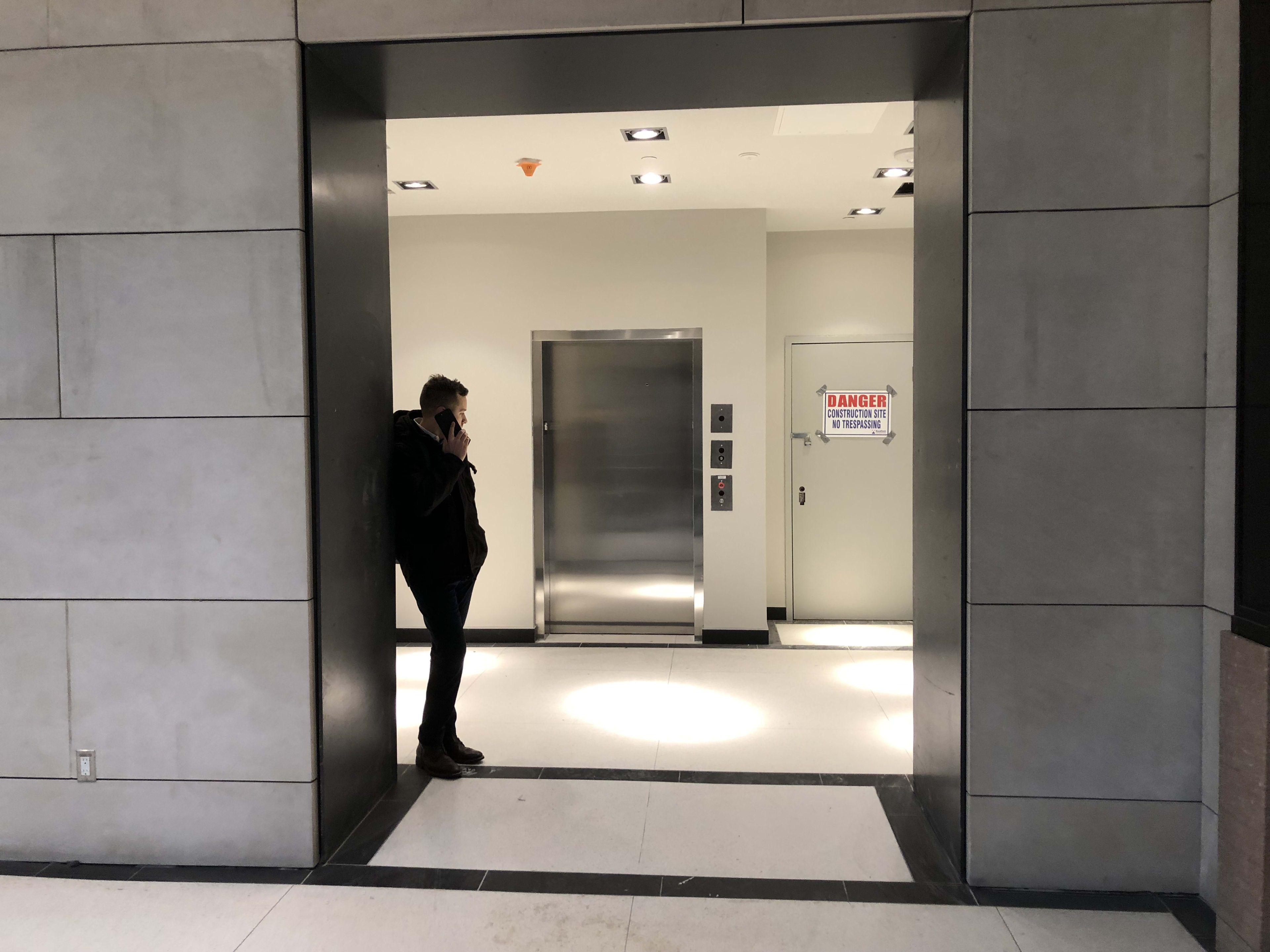 A man talks on the phone next to an elevator.