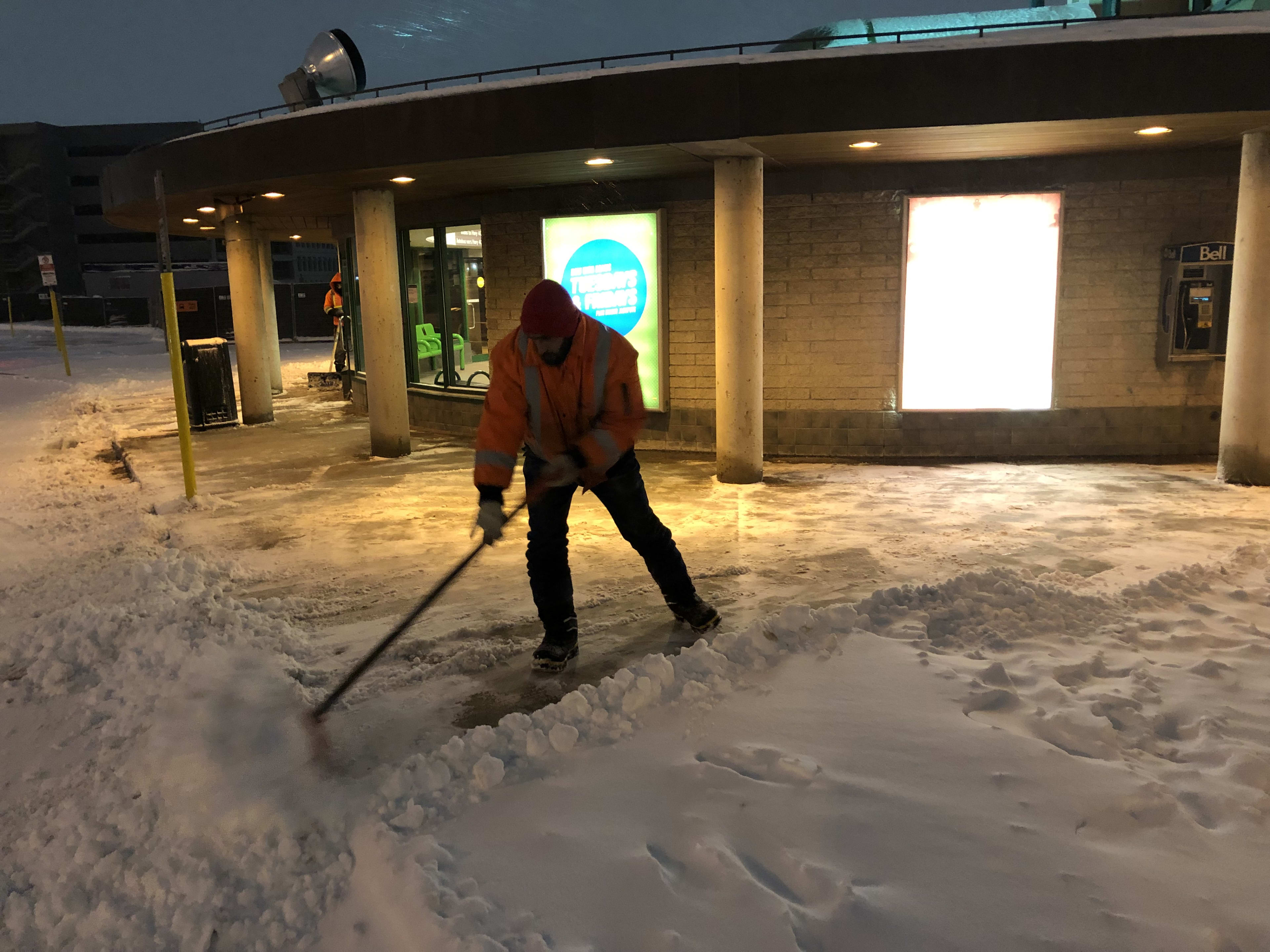 A man moves snow on a walkway in the early morning.