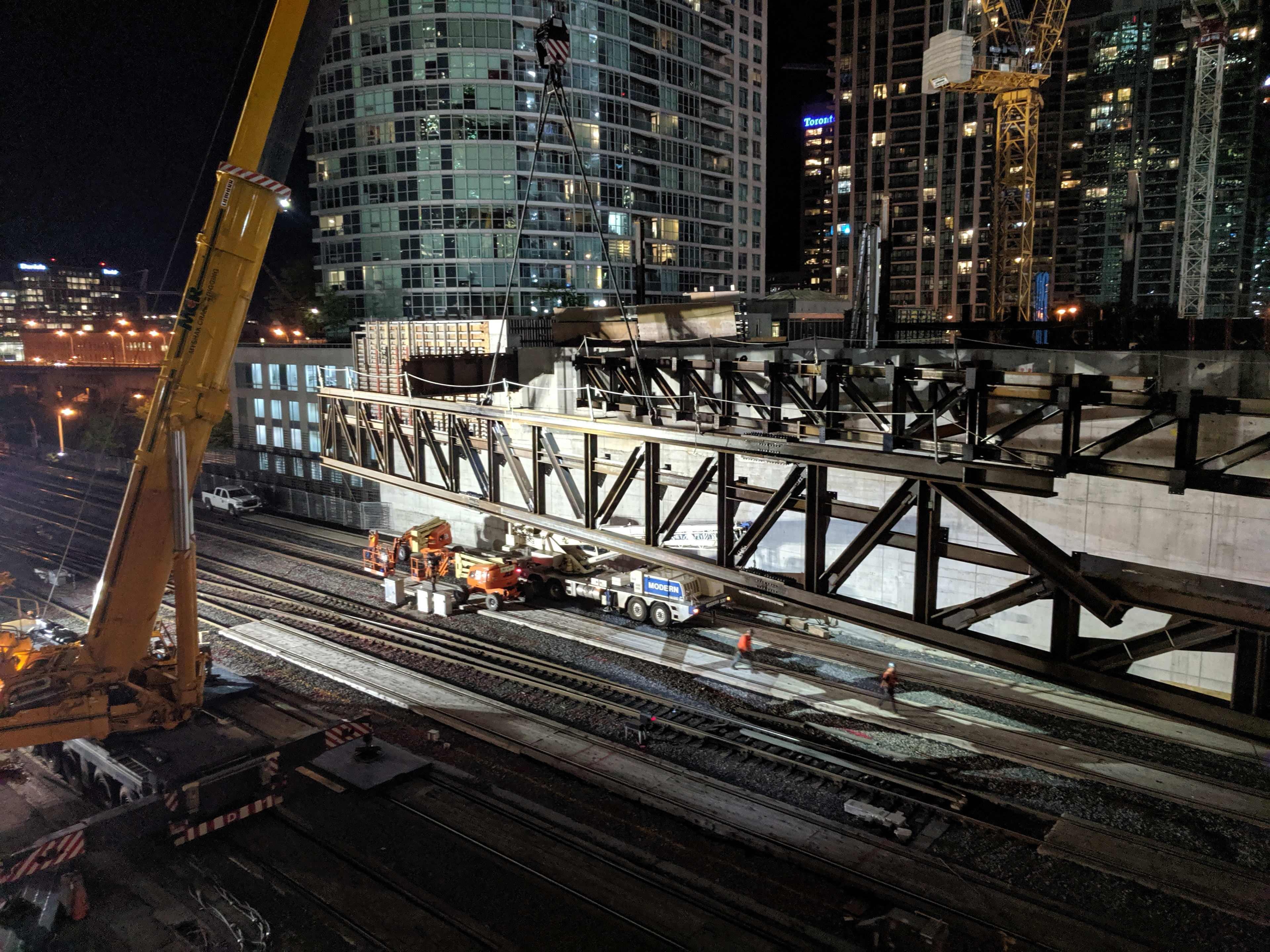 A powerful crane lifts the massive metal truss over the tracks.