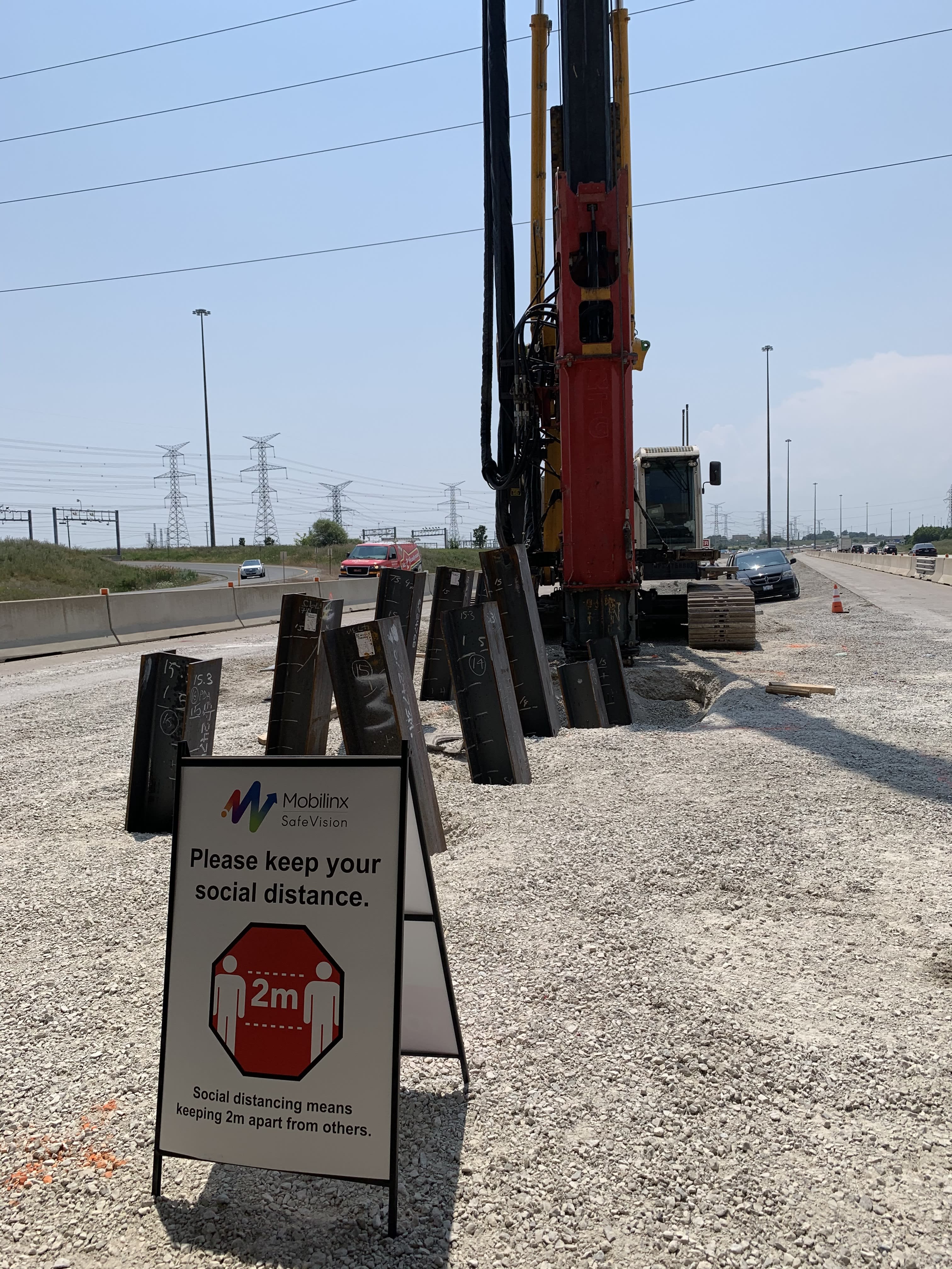 A sign reminding workers to keep two metres apart stands in front of a piece of machinery.