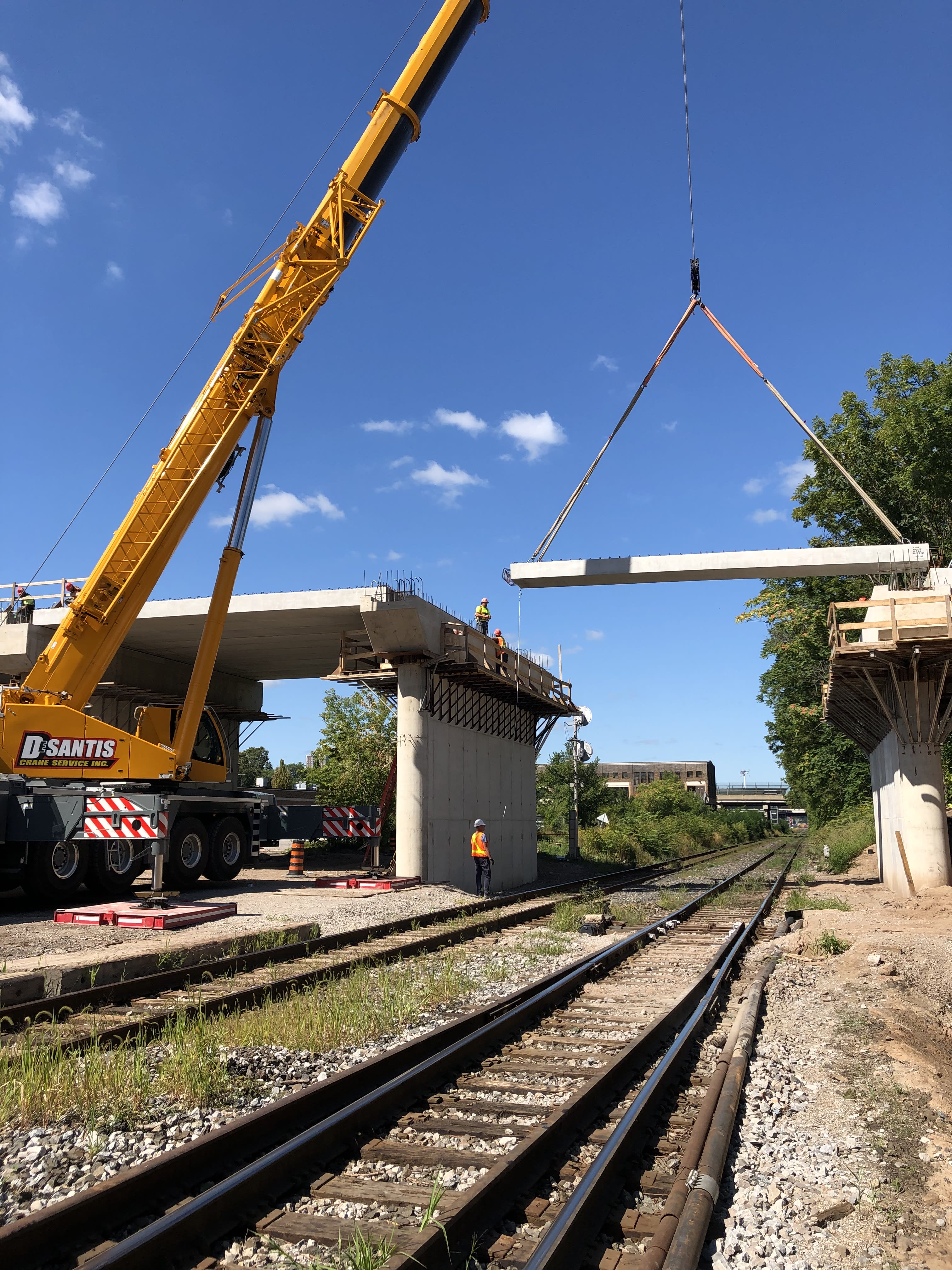 A large piece of concrete is lowered into place as part of a bridge replacement over top of train...