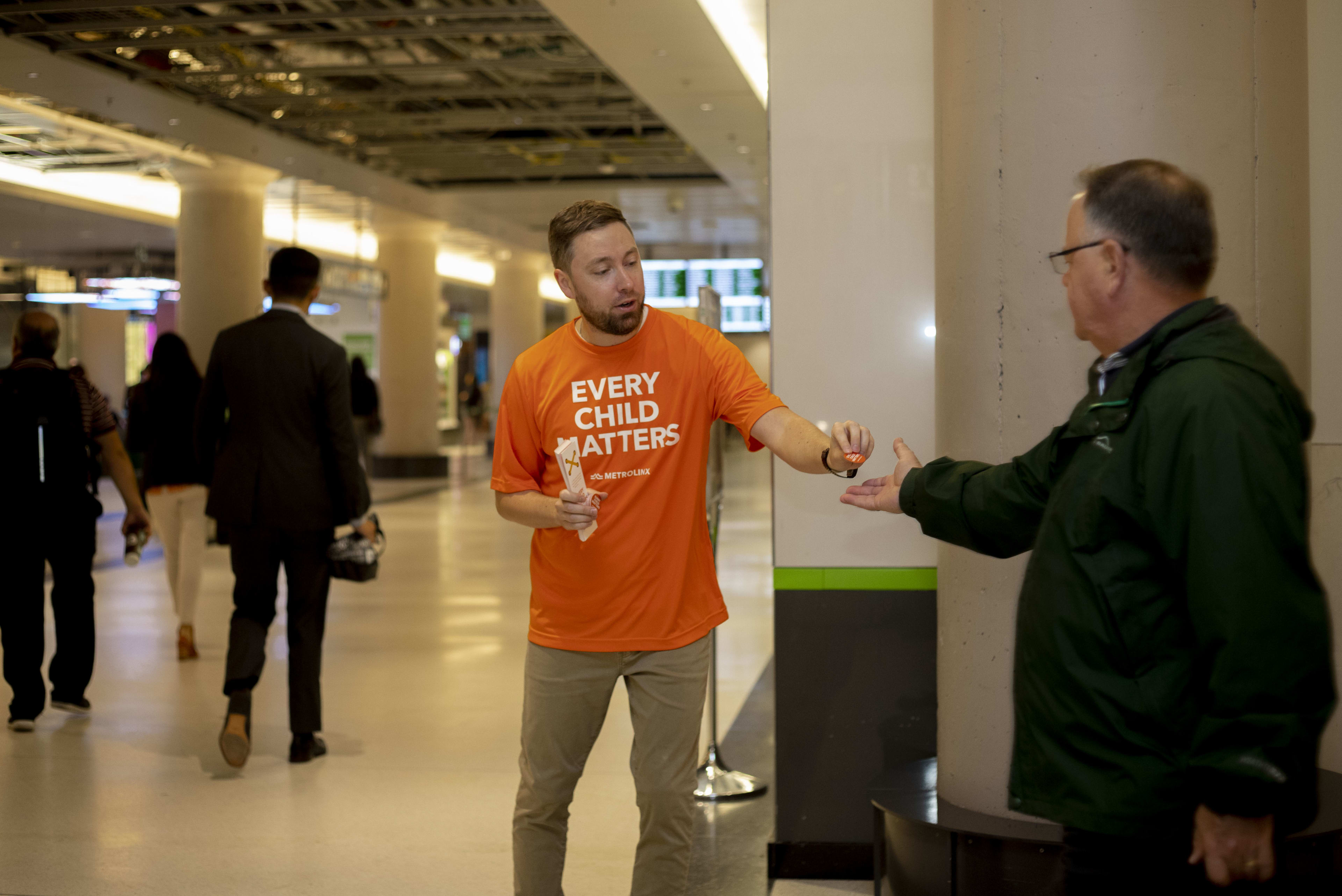 A volunteer hands out a Orange Shirt Day sticker.