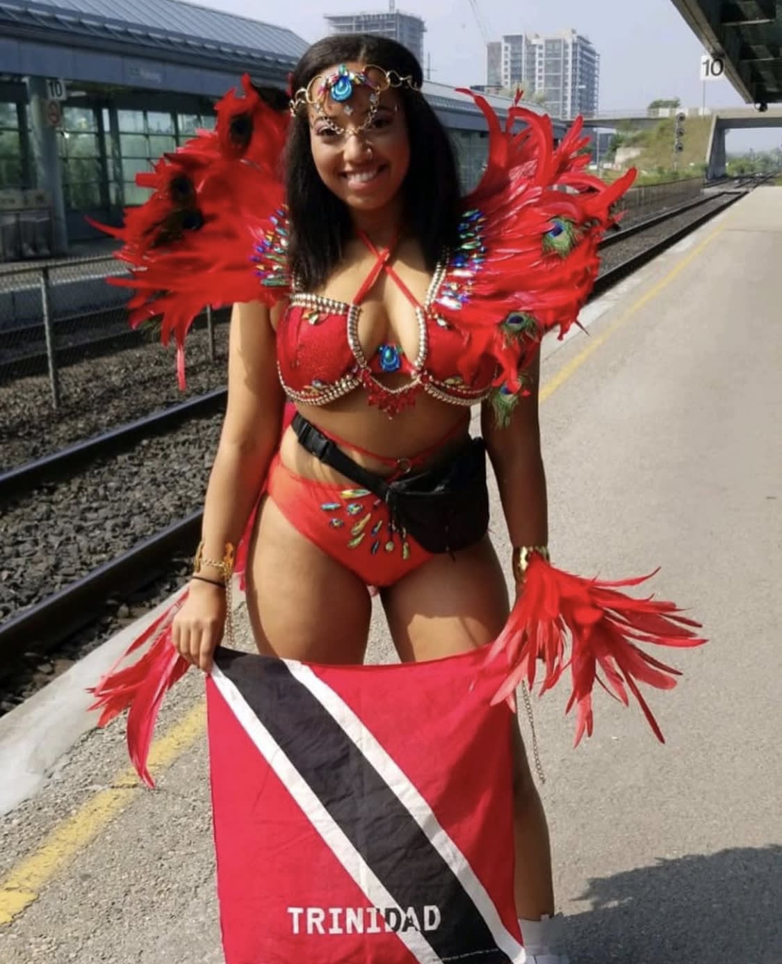 A young woman stands on a train platform while wearing a vibrant costume.