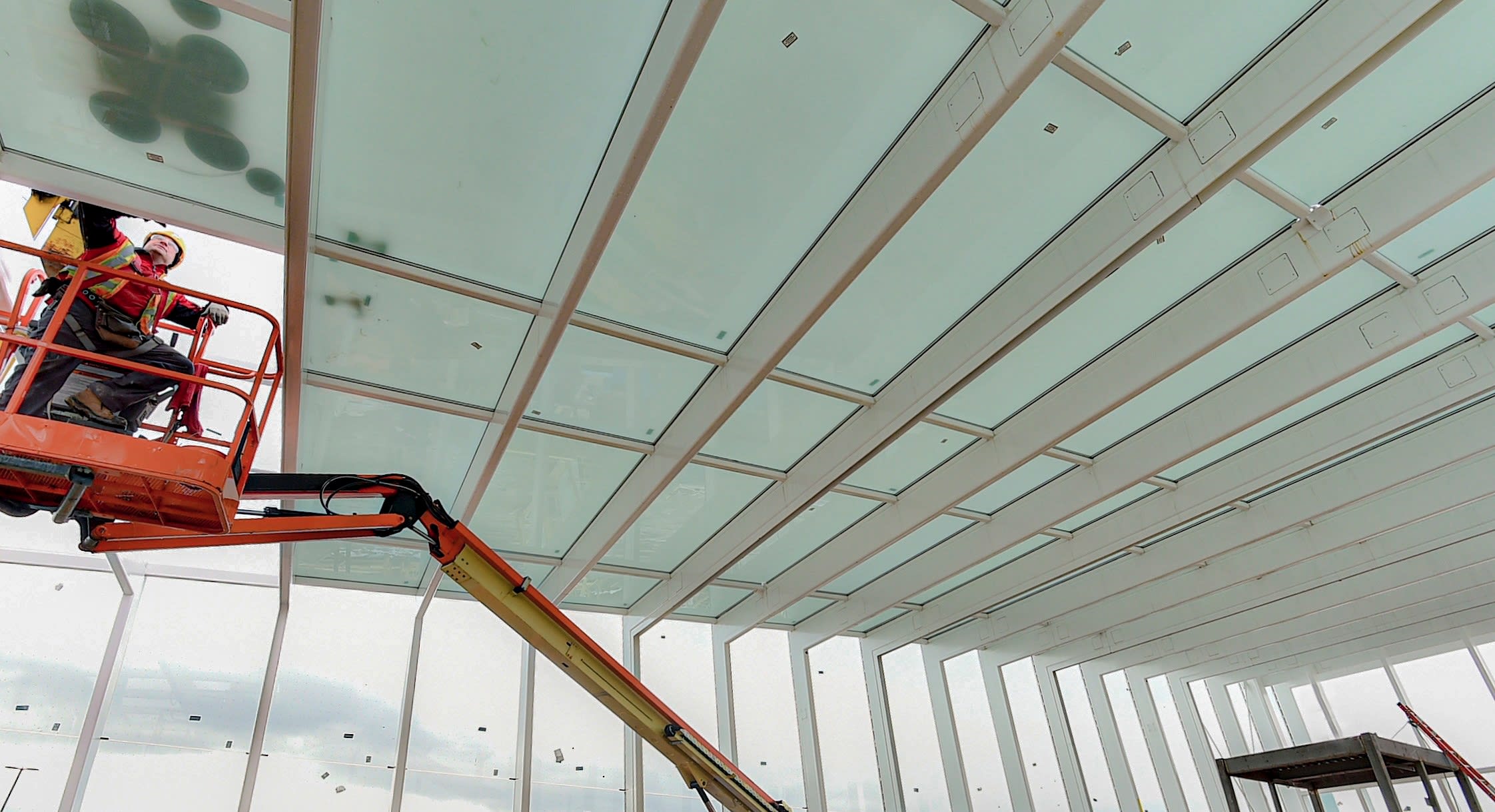 A worker is lifted by a cherry-picker to help install glass.