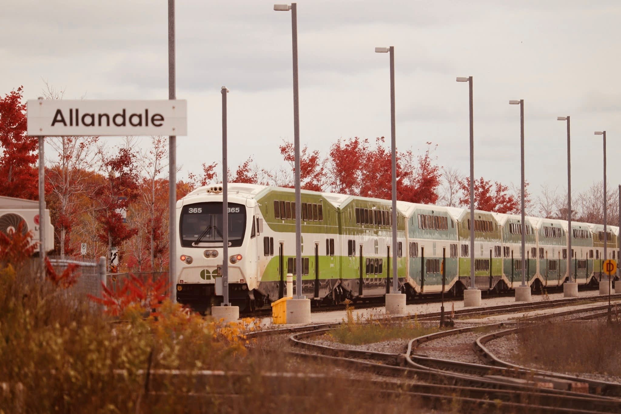 A GO train moves along tracks, with fall colours nearby.