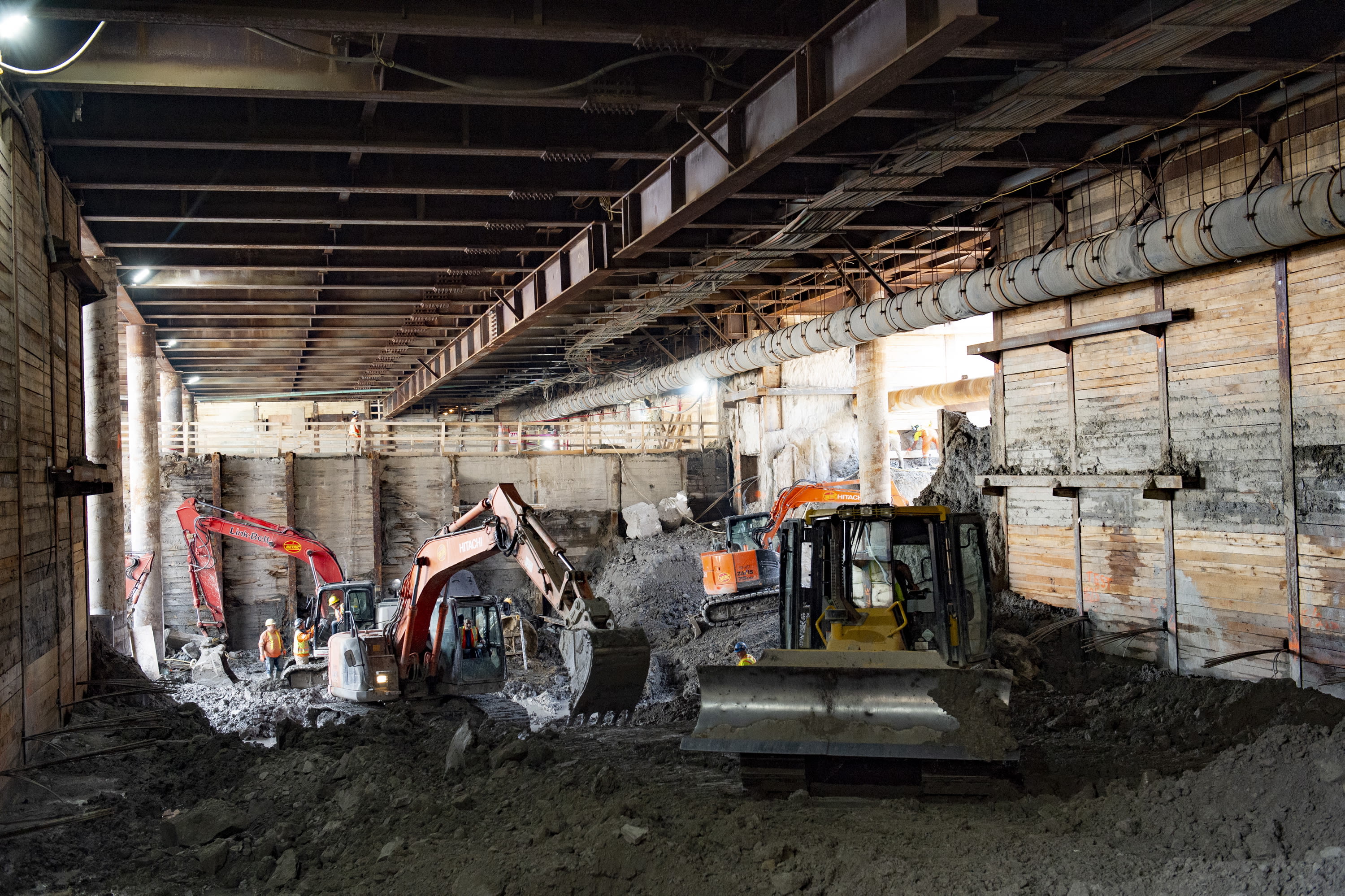 Tractors and crews work in a large pit, under a ceiling of wood and metal.