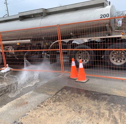A large water truck sprays a work area to remove dust and debris.