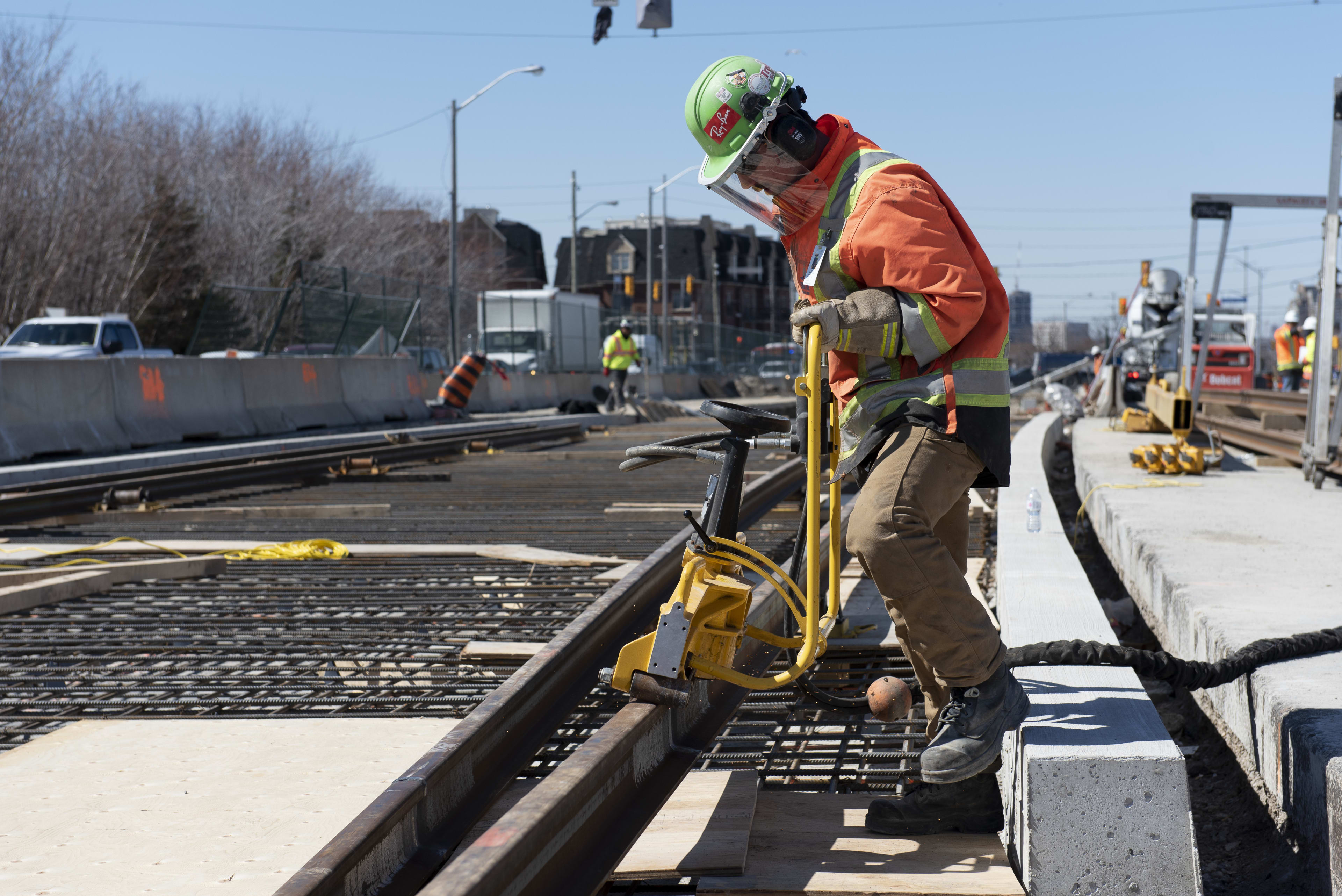 A crew meber uses a large tool to adjust a piece of track.