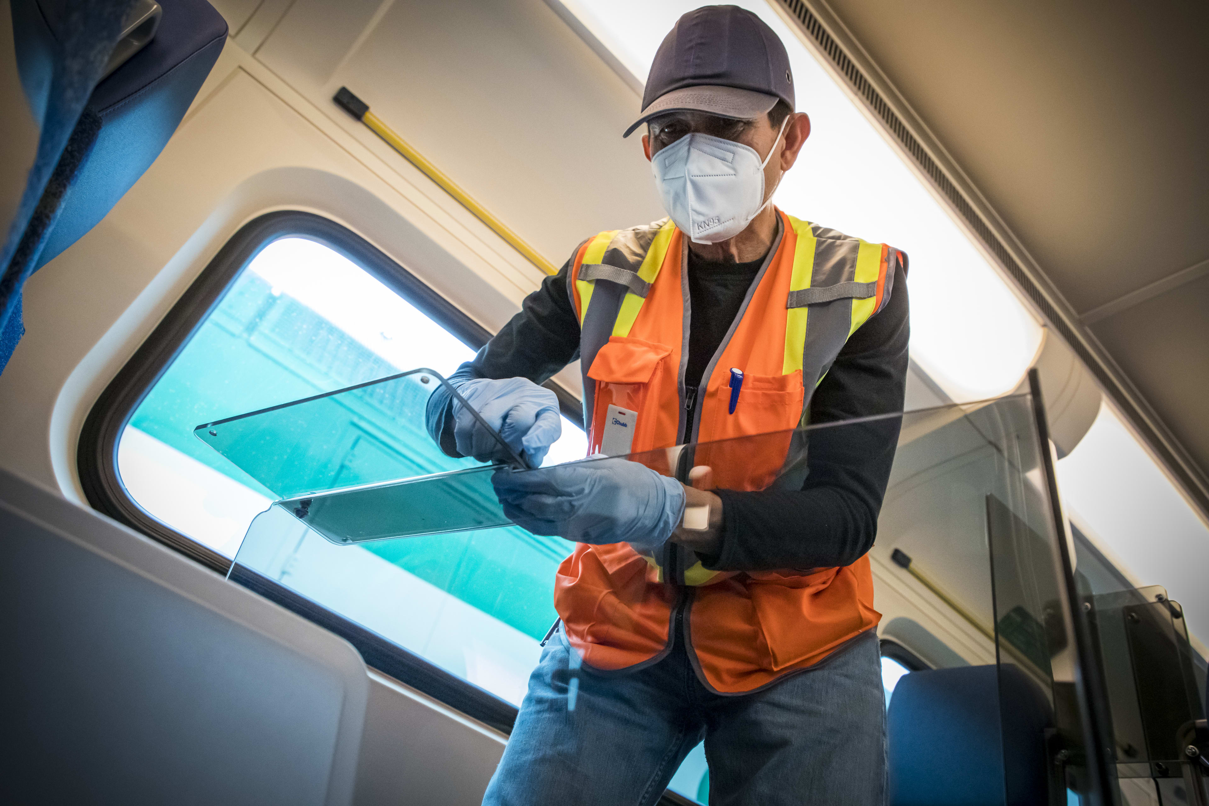 A man helps to attach a glass barrier next to a seat on a train.