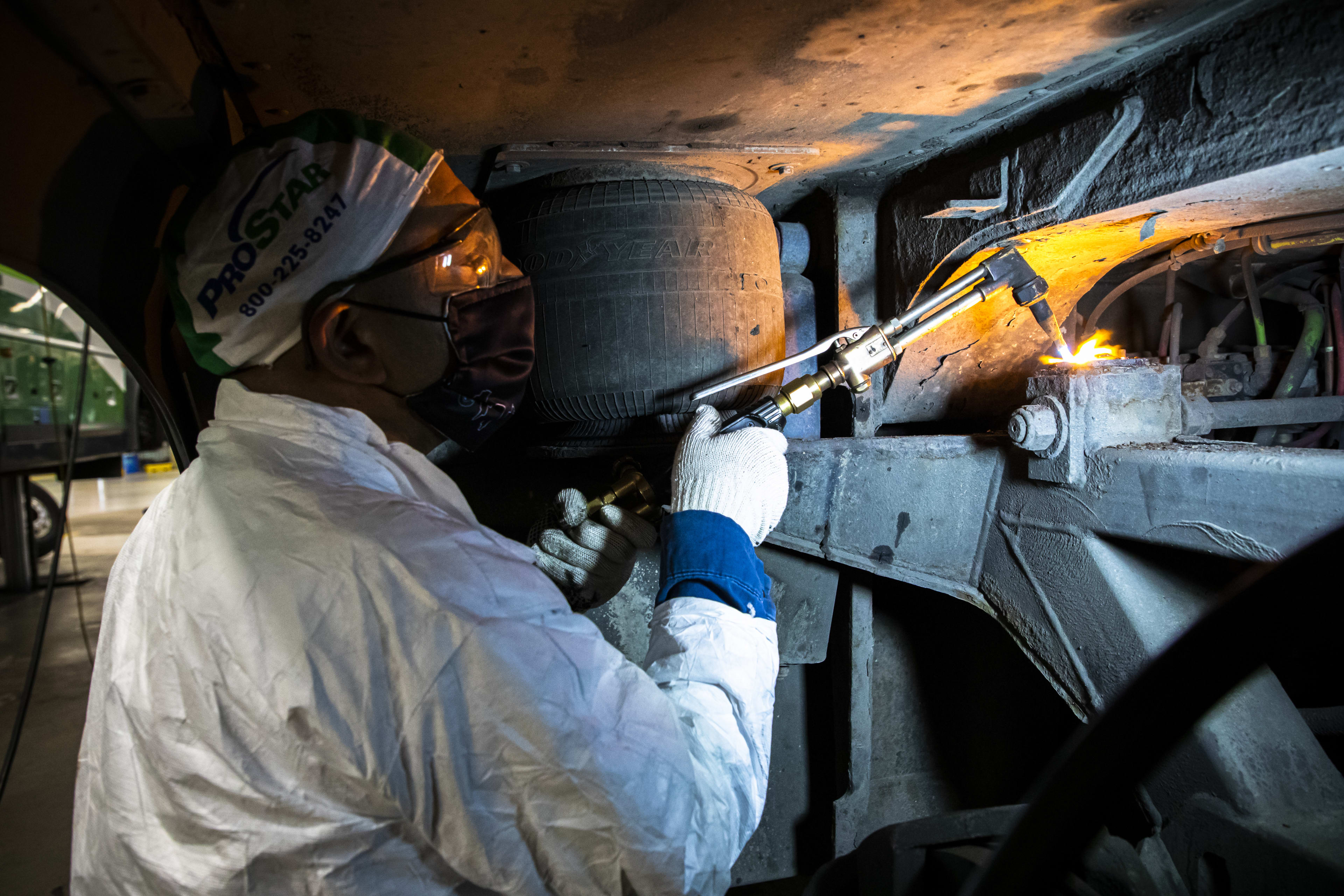 A worker uses a blow torch on bus part.