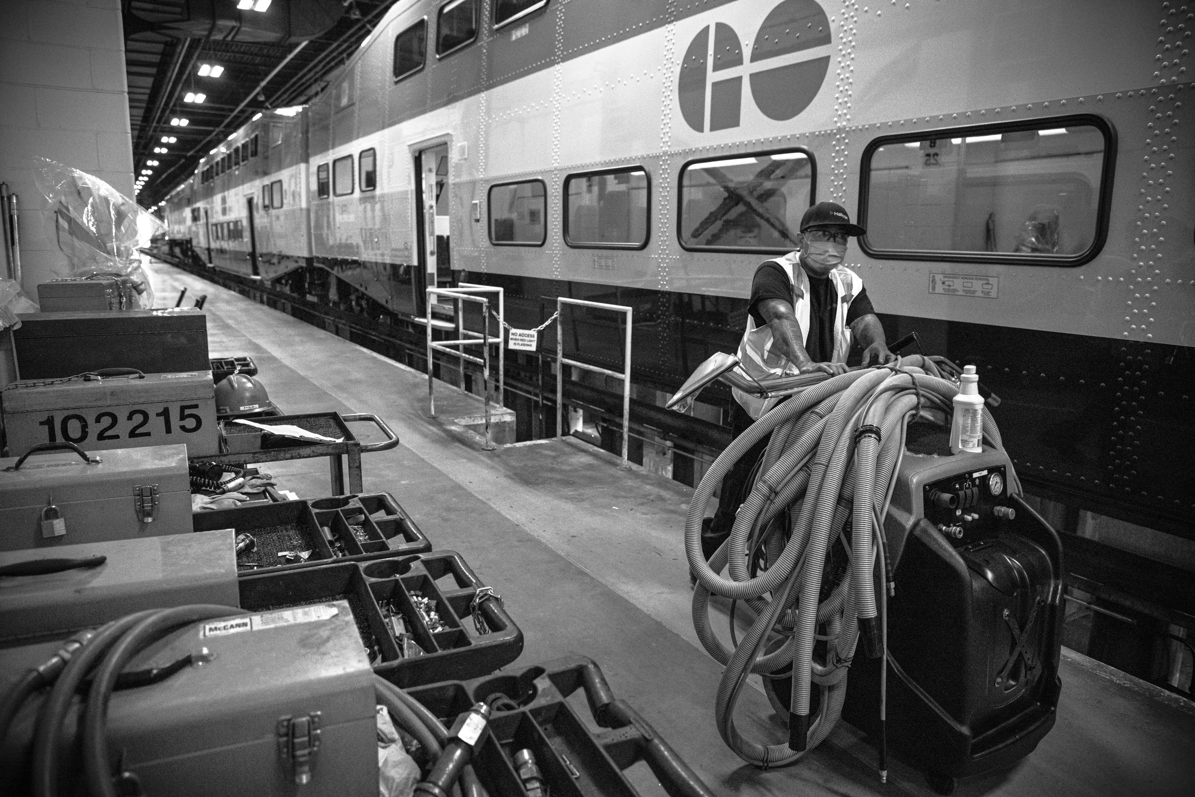 A worker carries cleaning tools next to a train.
