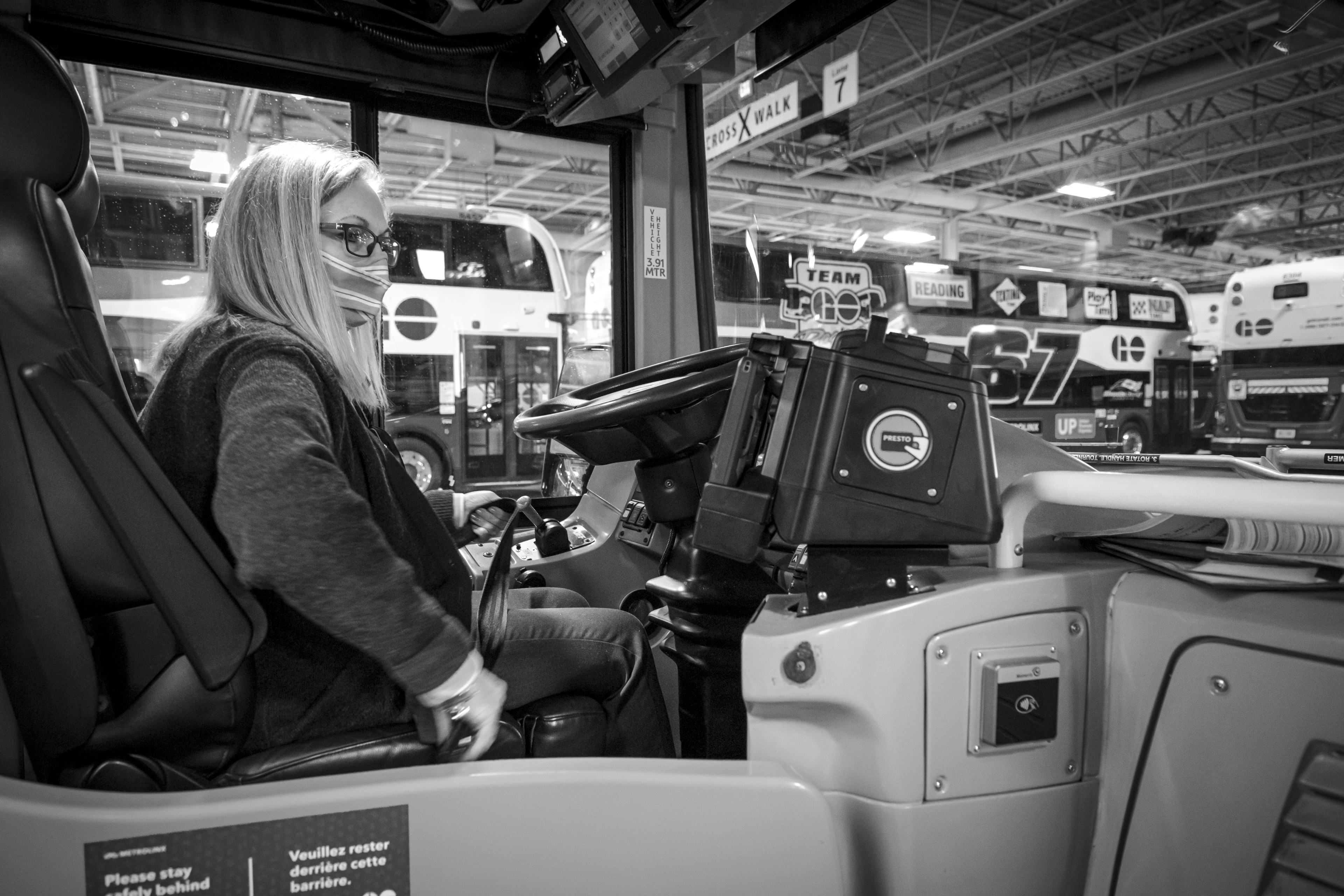 A woman sits at the driver's seat of a bus.