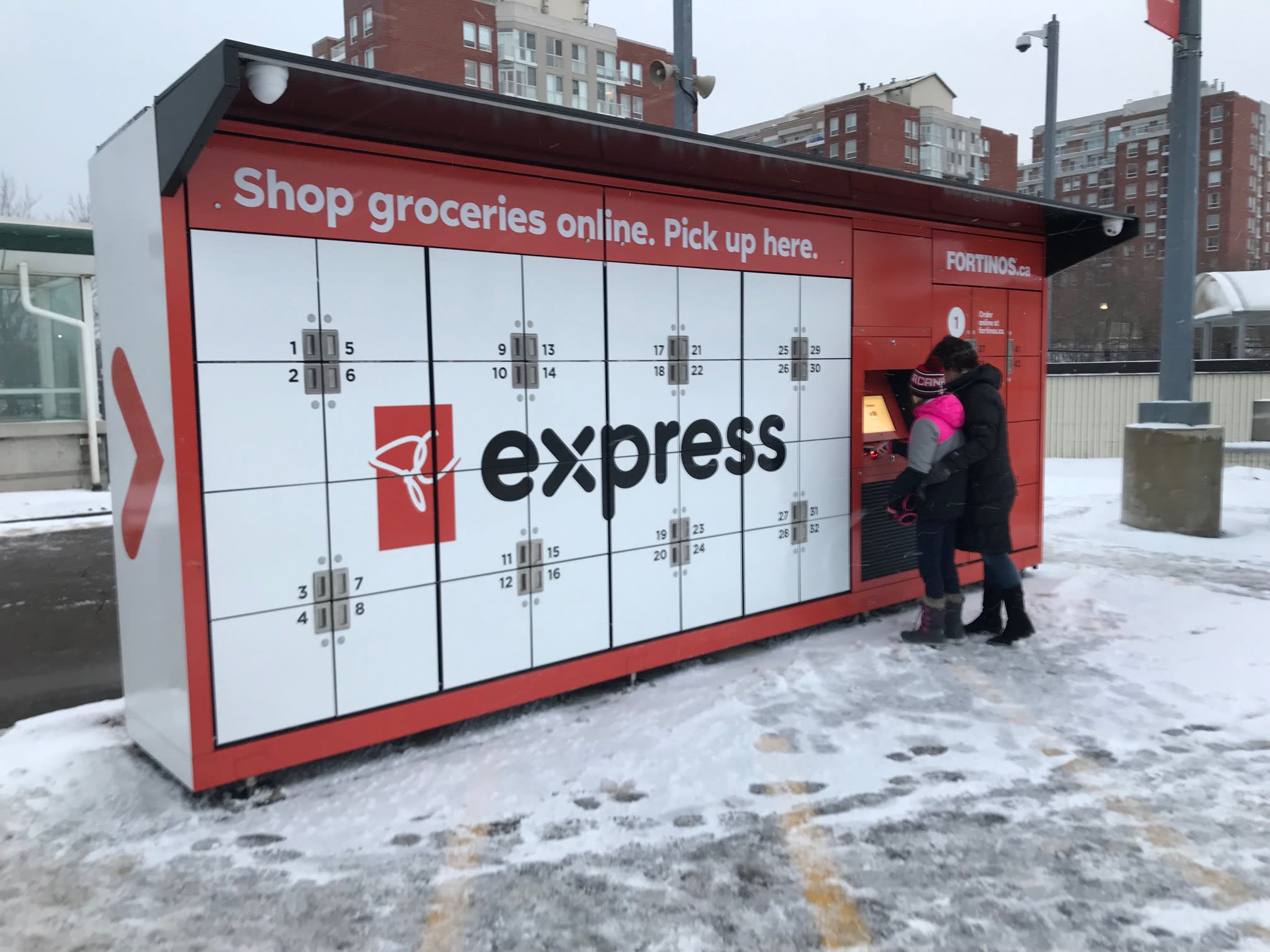 Two people stand in front of a group of lockers at a GO station.